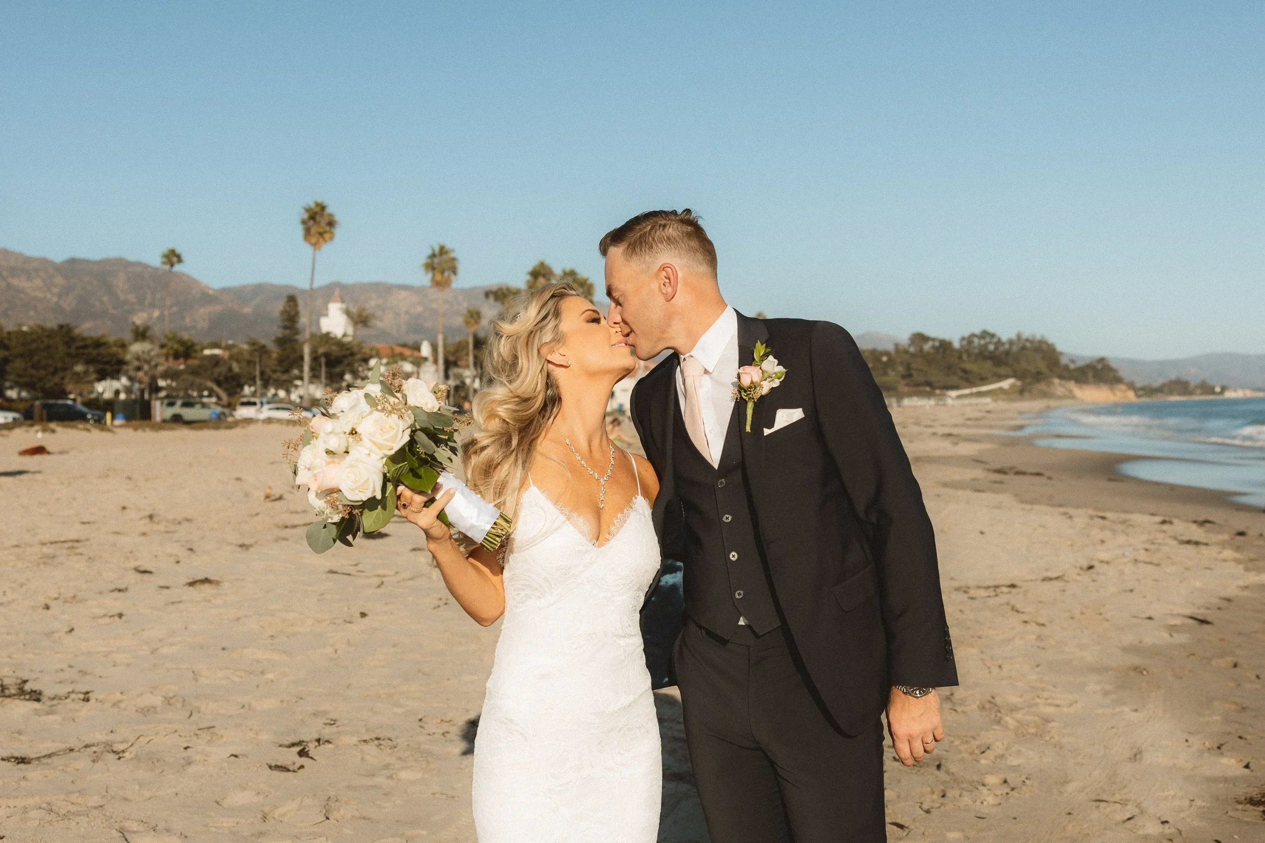Lauren and Dane sharing a romantic kiss on the sand with the Santa Barbara mountains in the background during their Mar Monte Hotel wedding.