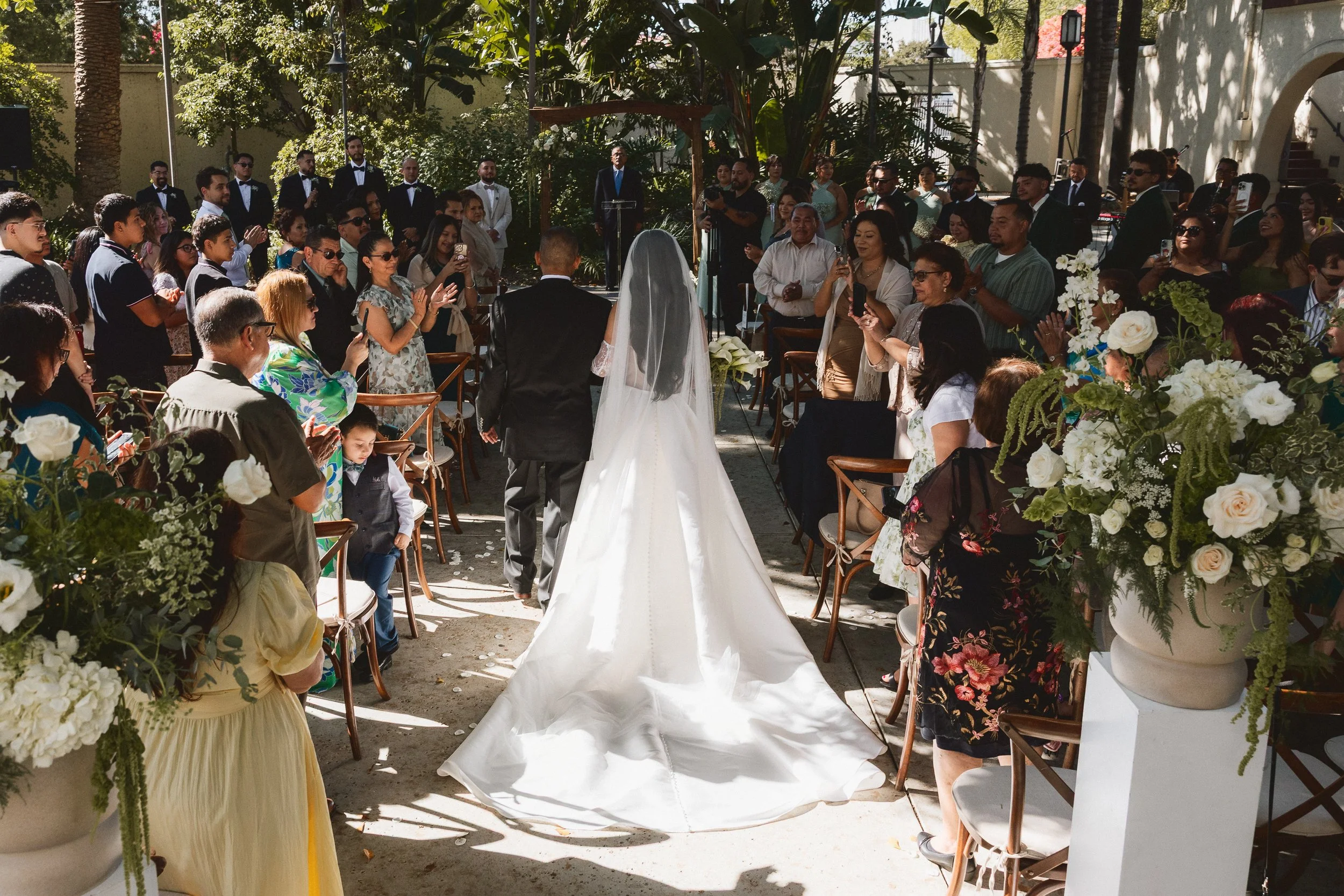 Bride and father walking down the aisle surrounded by guests and floral arrangements