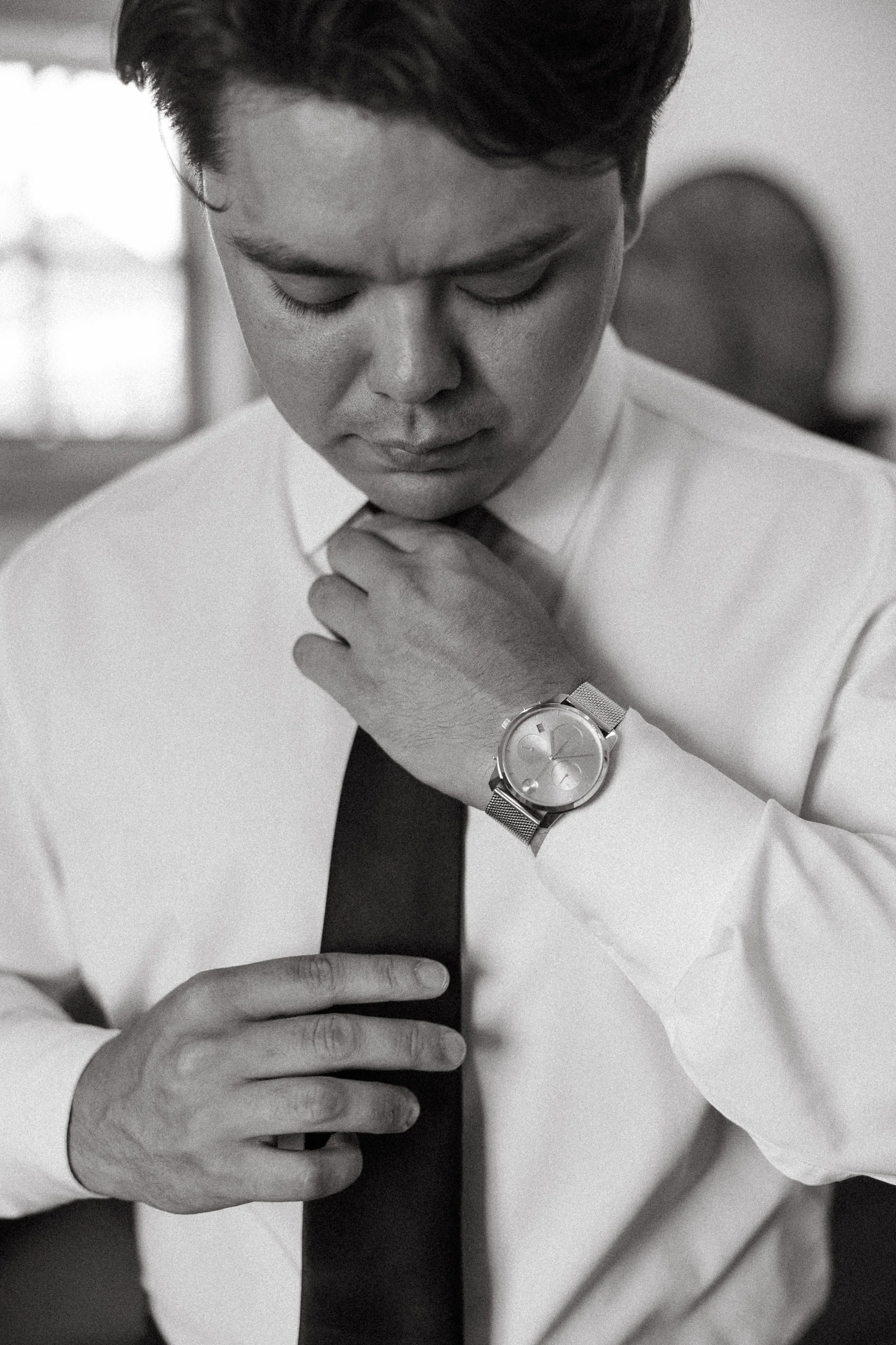 Groom adjusts his tie while getting ready in black and white