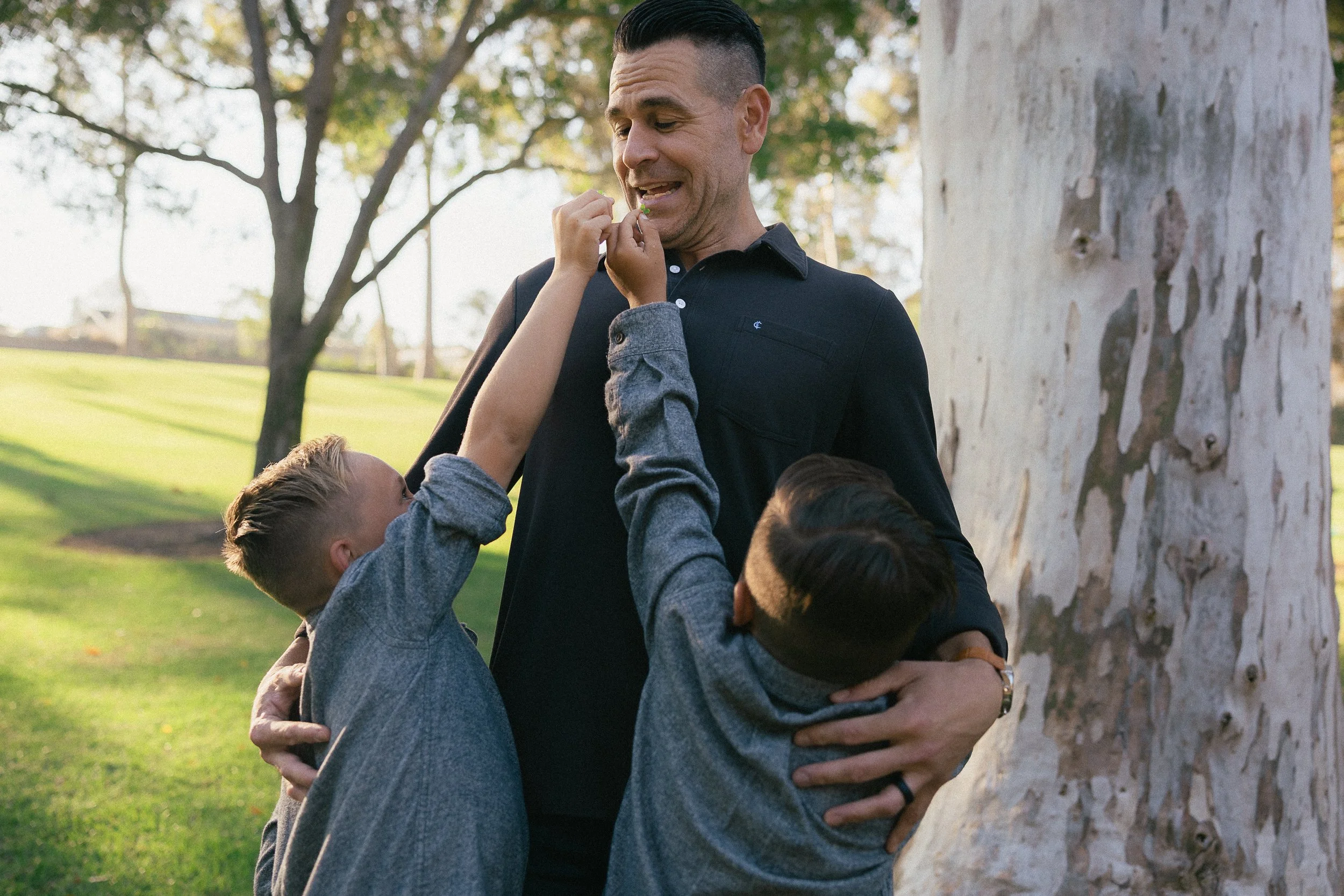 Dad reacting while his two sons playfully reach up toward his face.