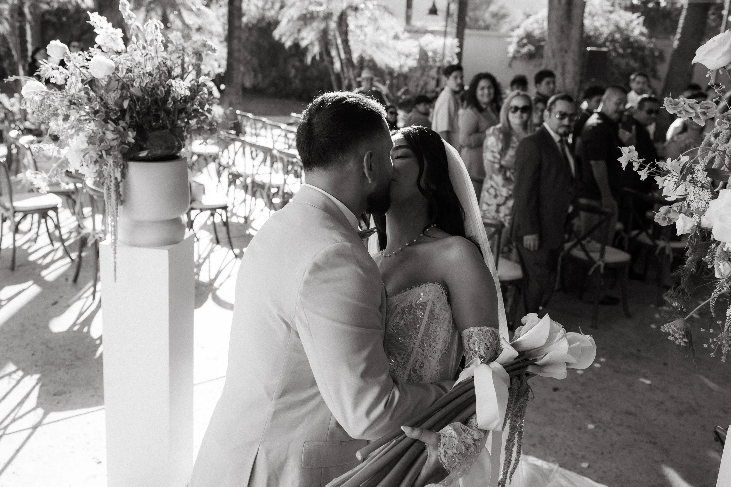 Bride and groom kissing at the end of the aisle surrounded by wedding guests at Los Angeles River Center and Gardens.