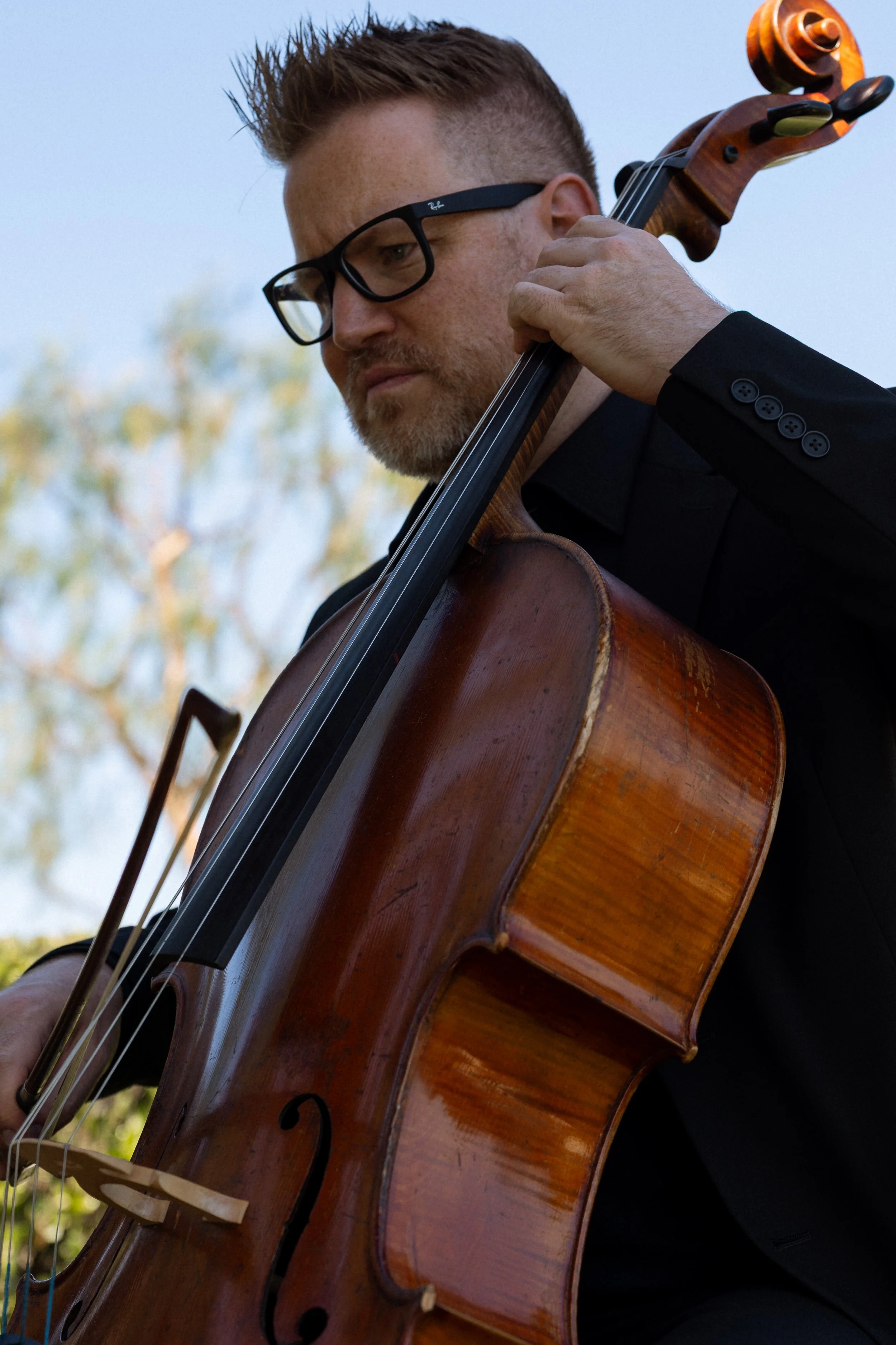 A cellist in glasses plays during the ceremony against a soft sky