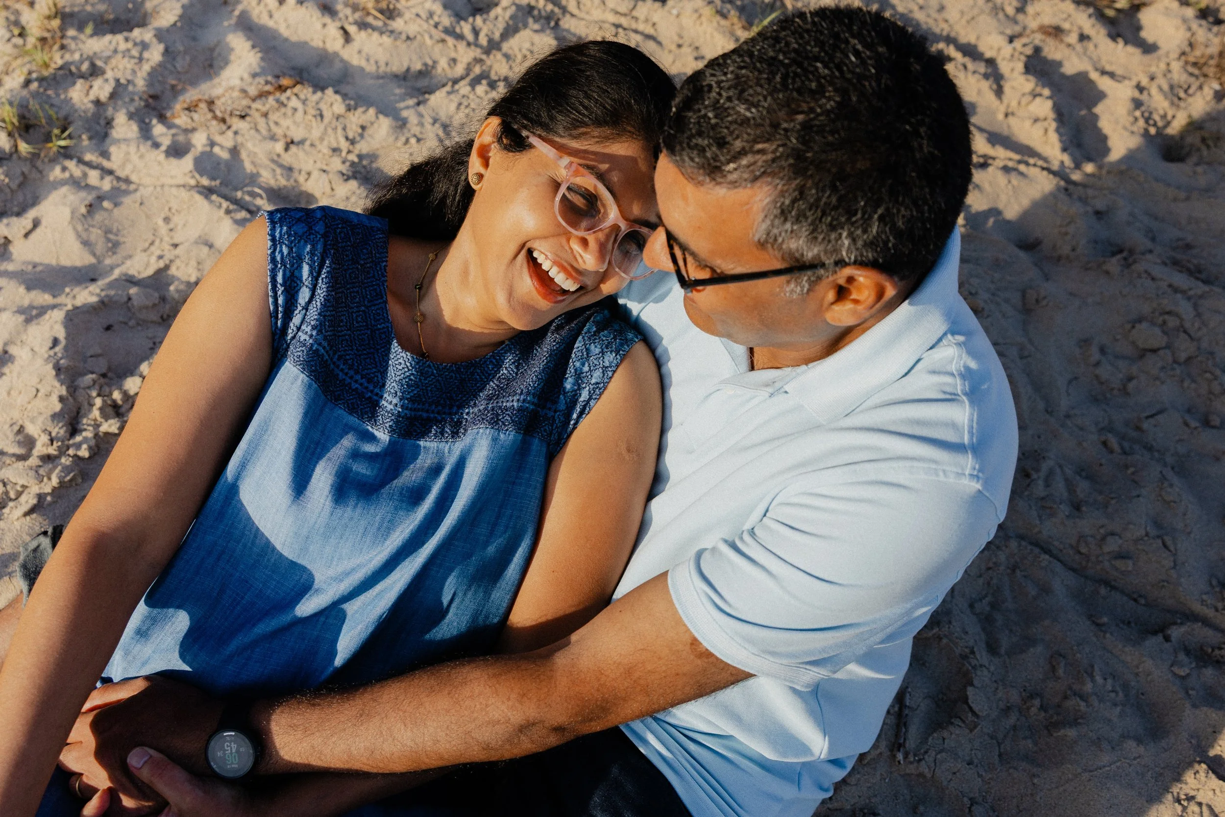 Couple sharing a joyful laugh while sitting on the sand during a family session at Crystal Cove State Park.