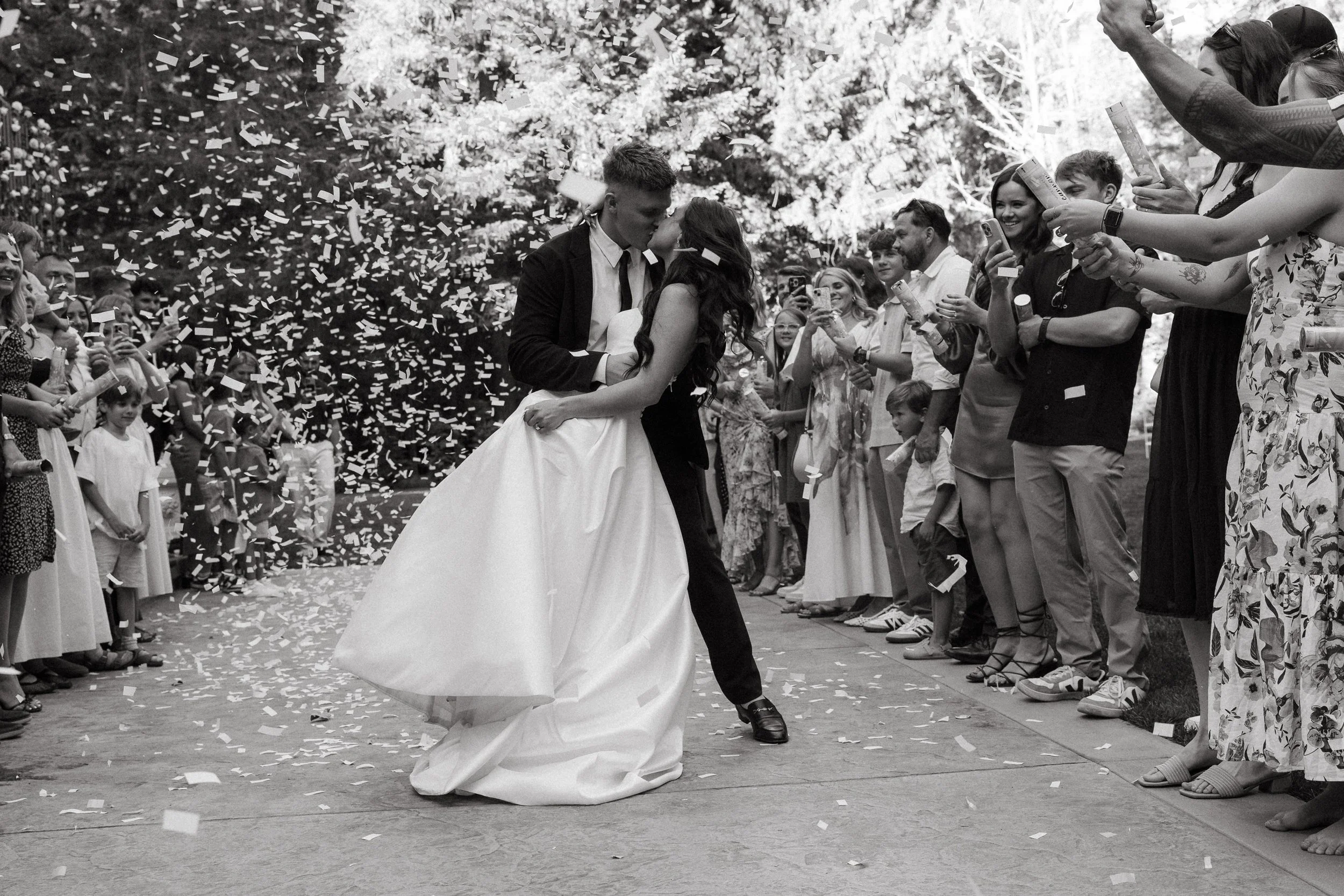 Groom dips the bride for a kiss as guests cheer and throw confetti during the exit