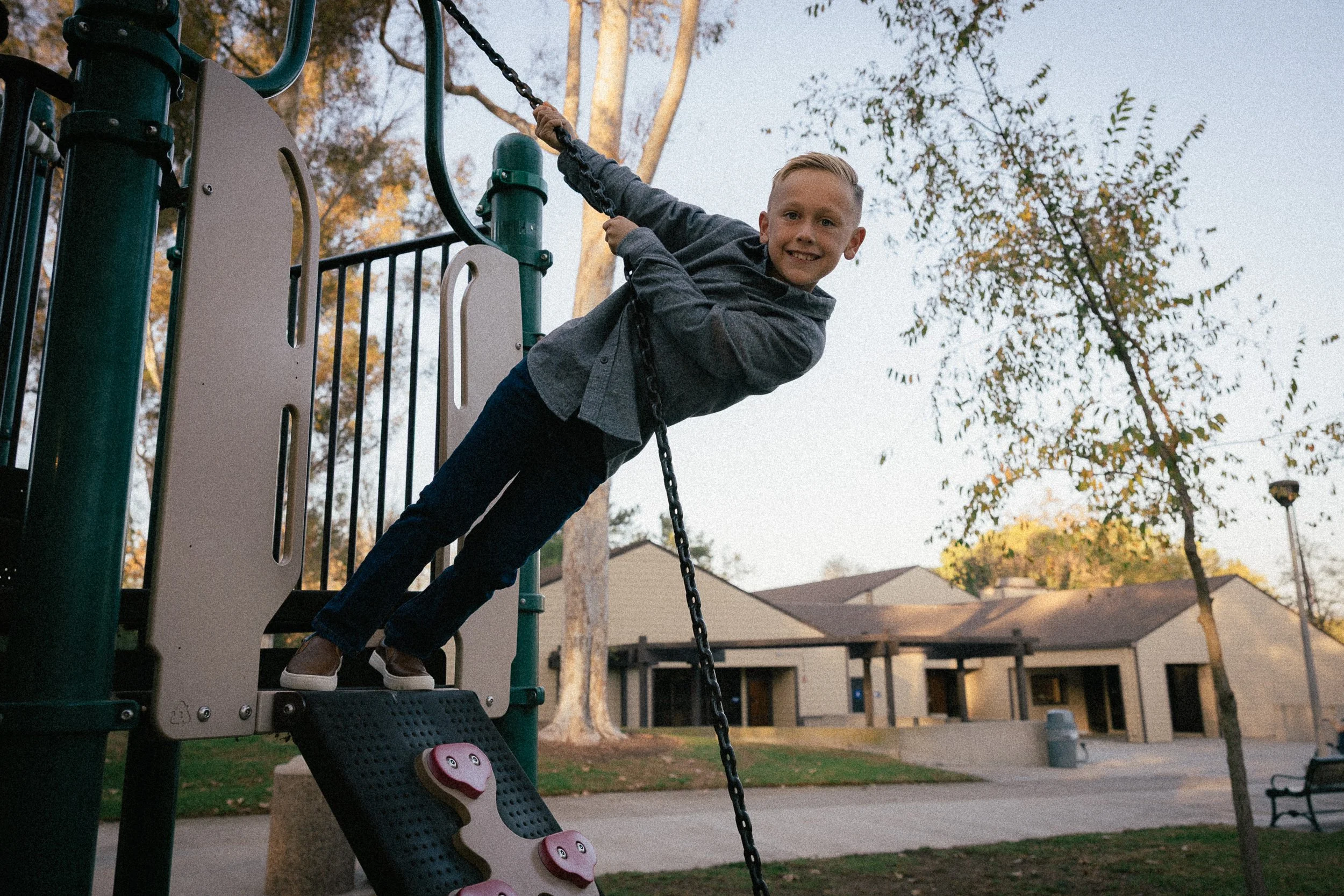Young boy leaning back while holding onto a chain at the playground.