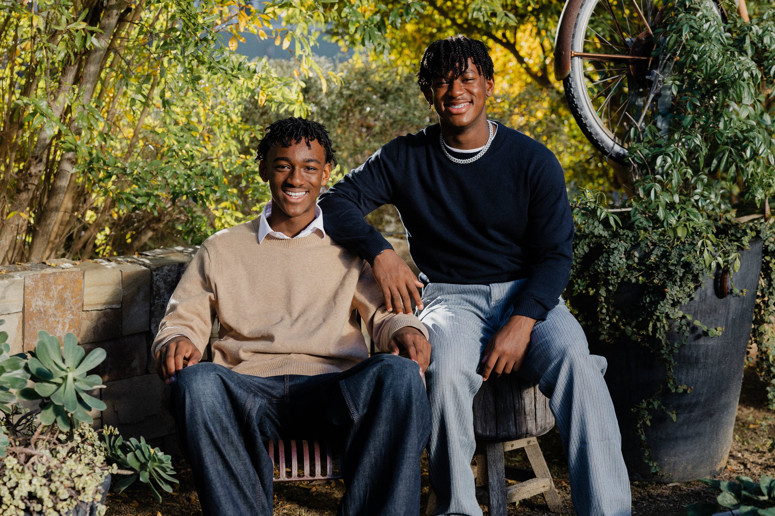 Two brothers smiling and sitting together on a garden bench surrounded by greenery in Irvine.