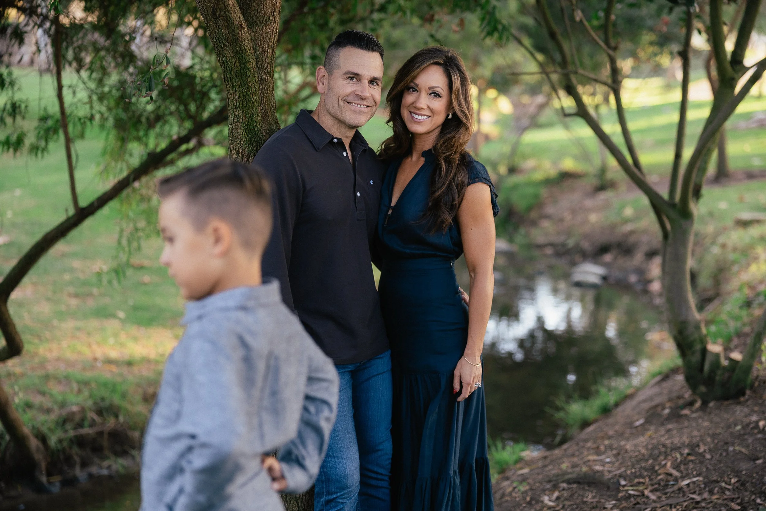 Mother and father standing by the creek while one of their sons walks in the foreground.