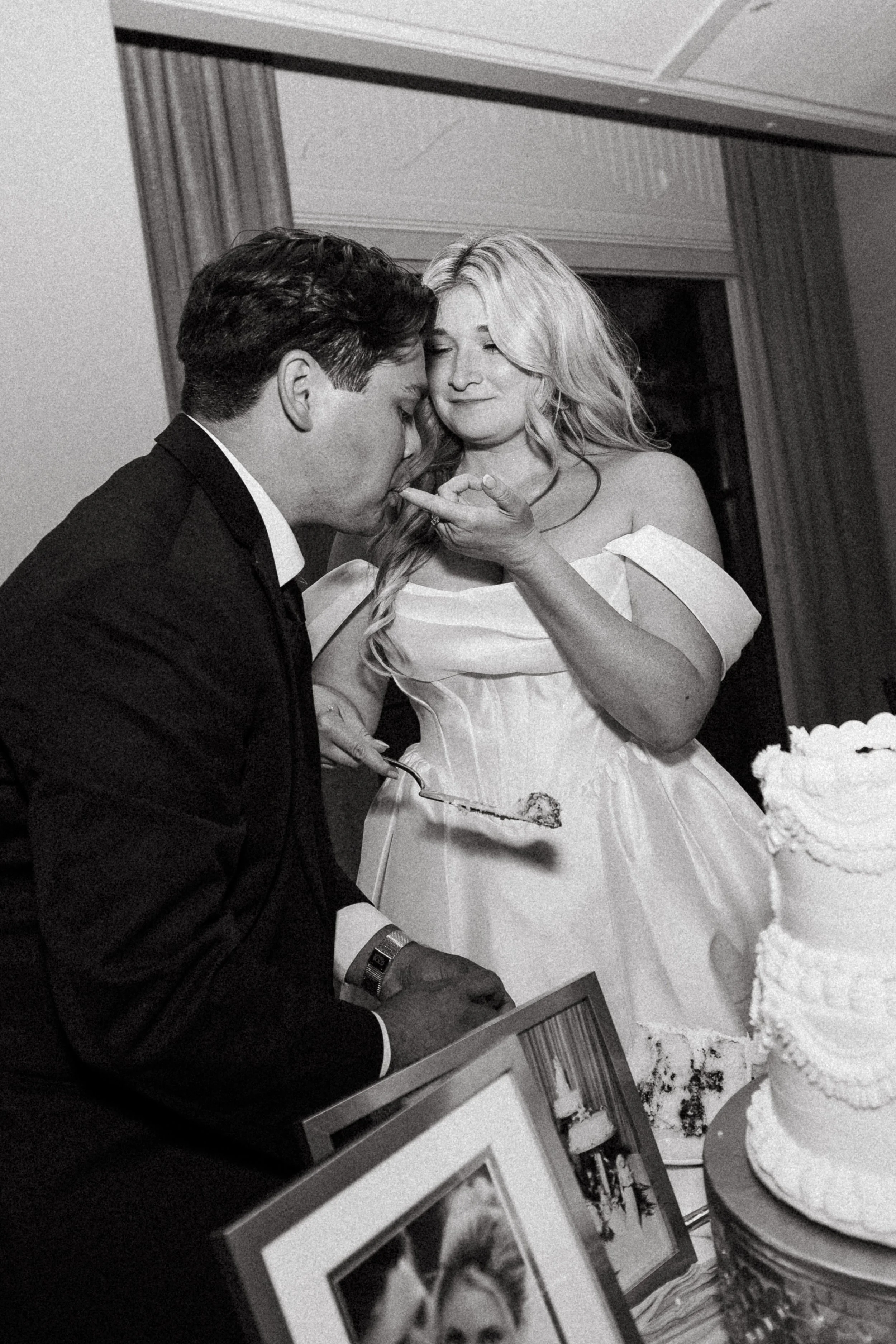 Groom kisses the bride's hand during the cake feeding in black and white