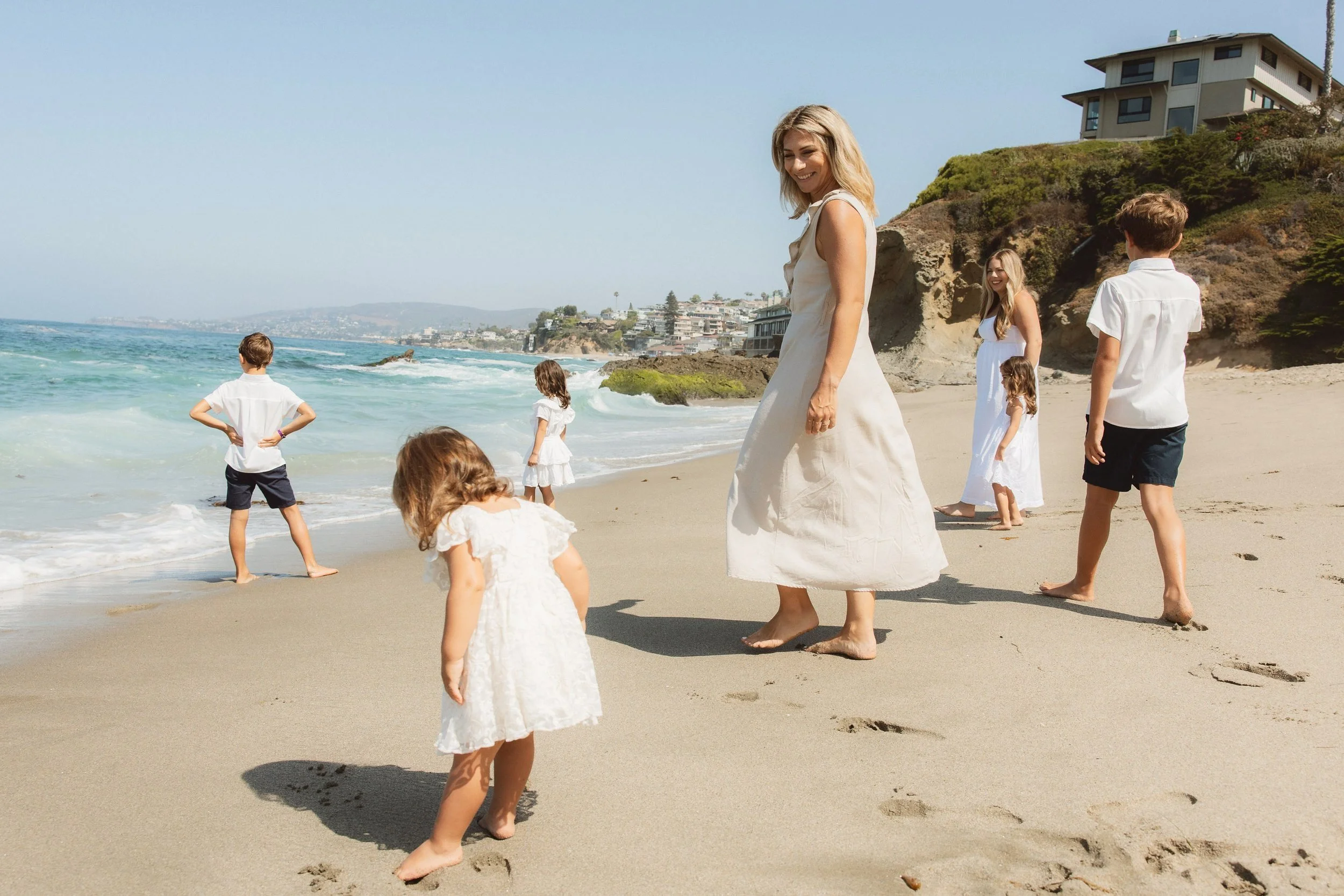 A mother walking barefoot on the sand with her children near the waves during a candid, bright family session at Treasure Island Beach.