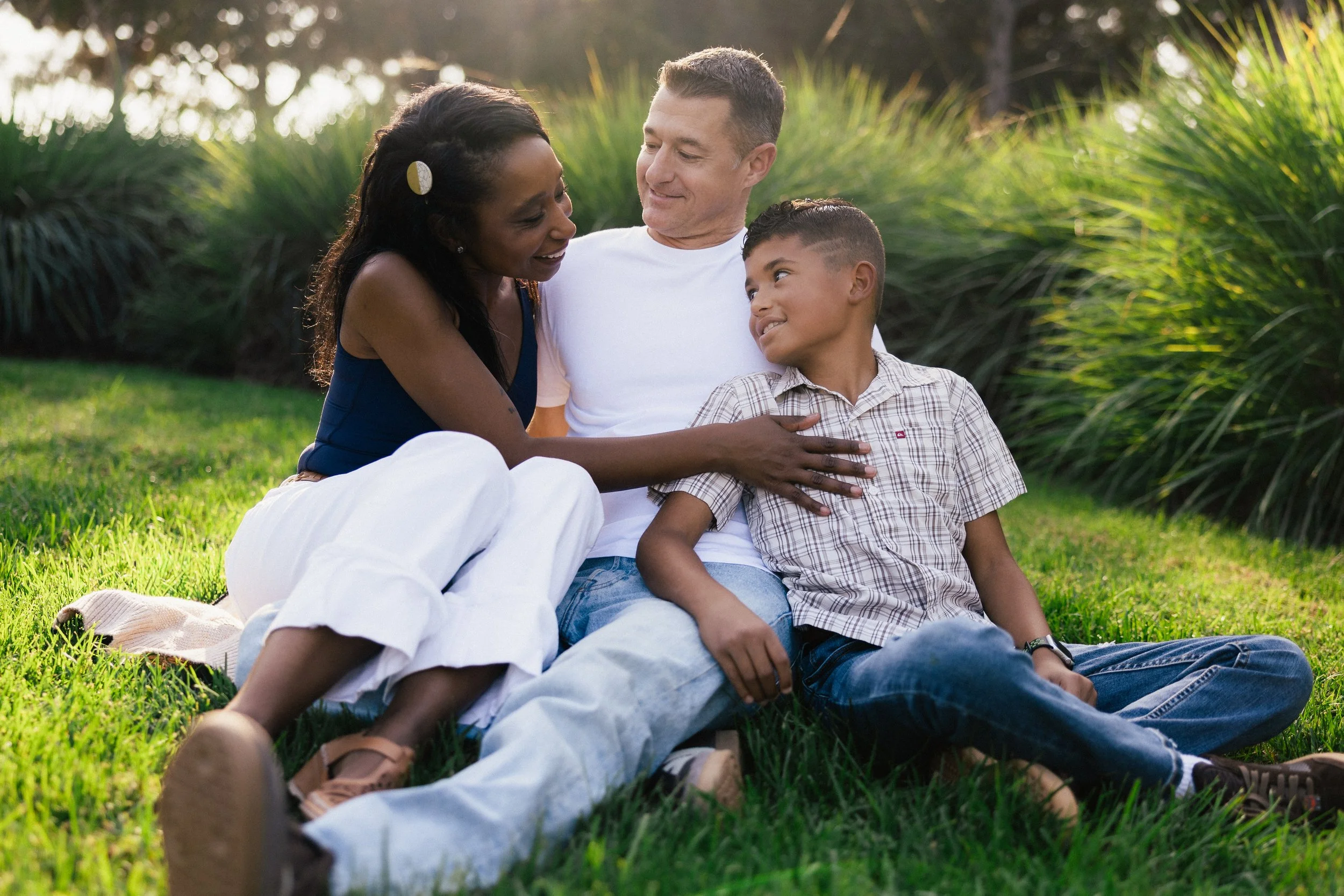 A mother, father, and son sitting together in the tall green grass at Jeffrey Open Space Trail in Irvine during a candid outdoor portrait session.