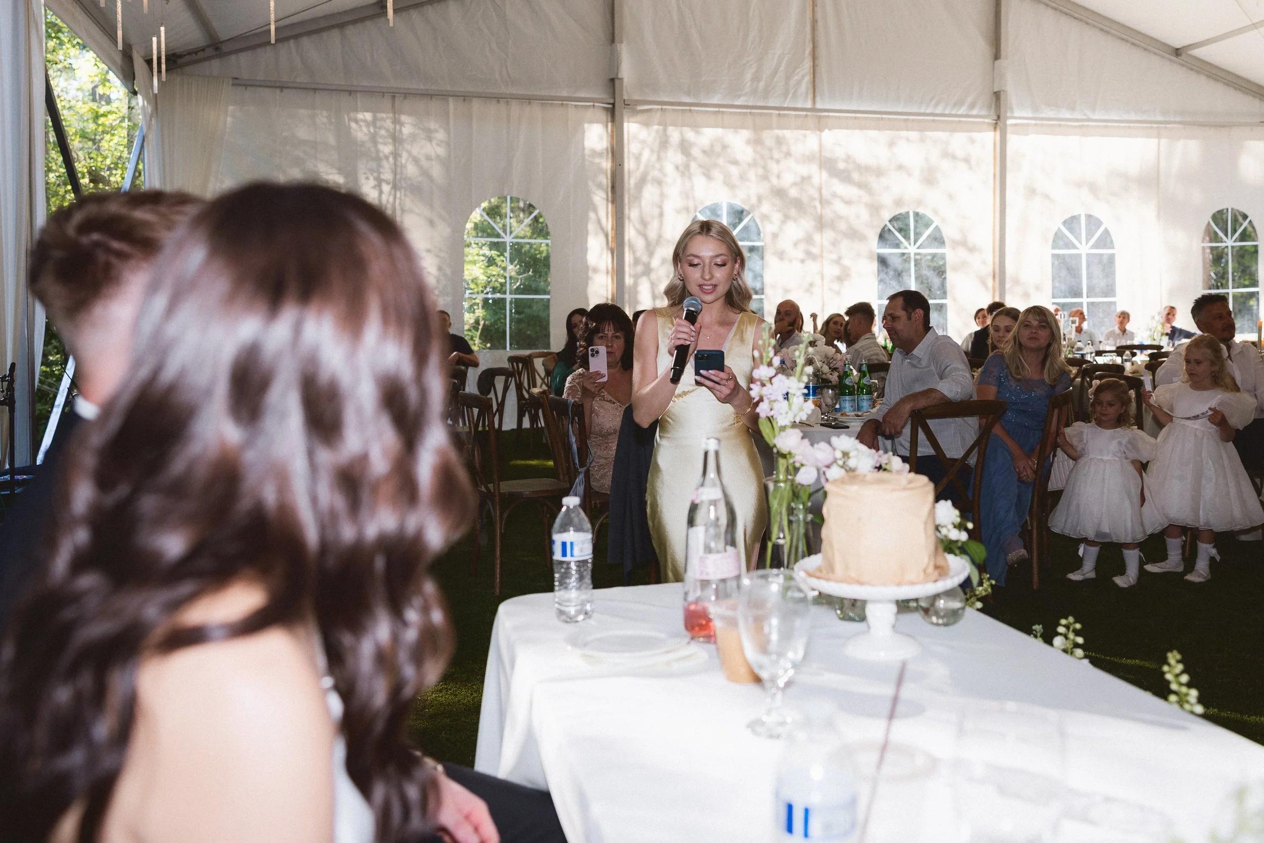 Maid of honor gives a speech while bride listens at the sweetheart table