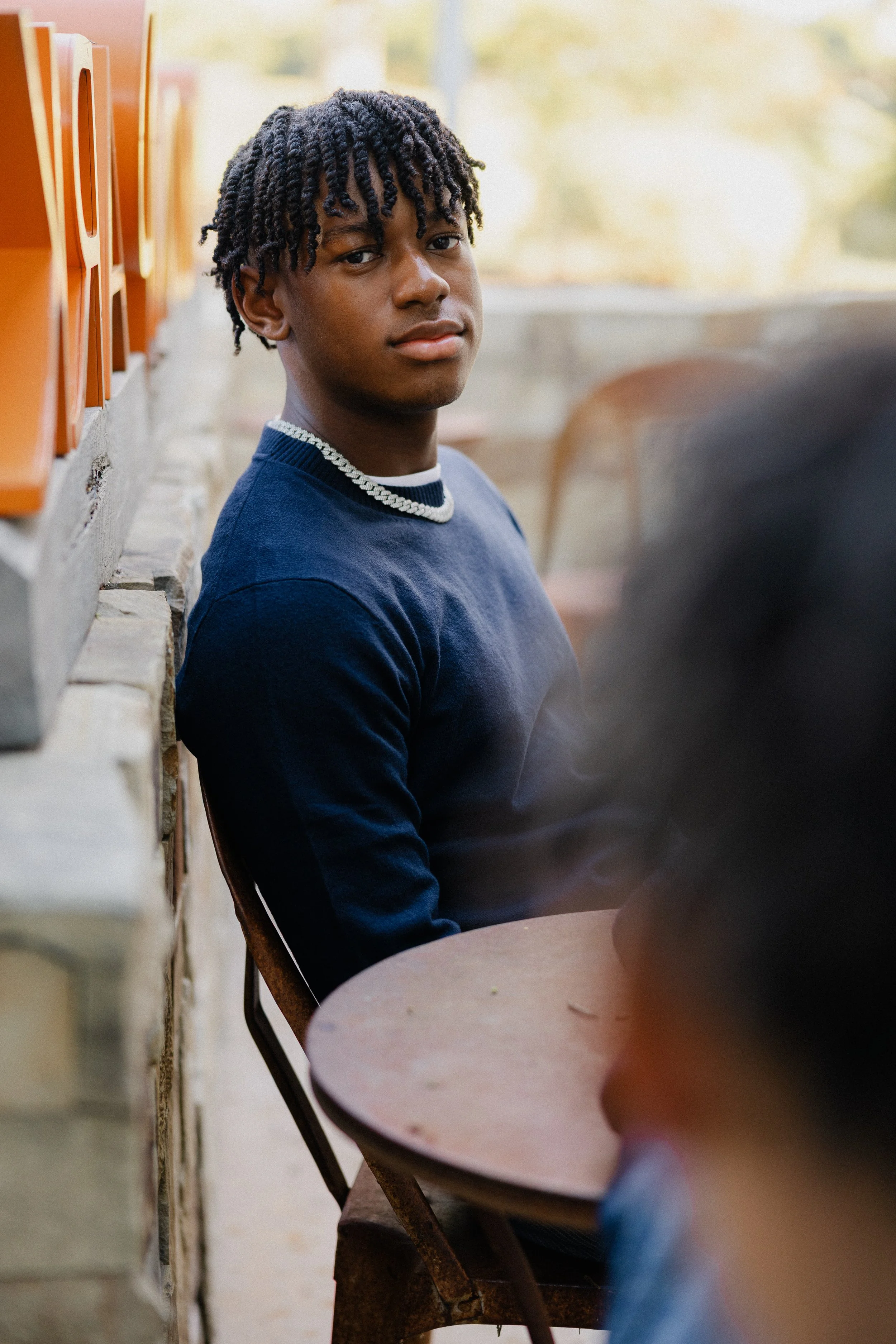 Teenage boy in a navy sweater sitting at a rustic table looking over his shoulder at Pavilion Park in Irvine.
