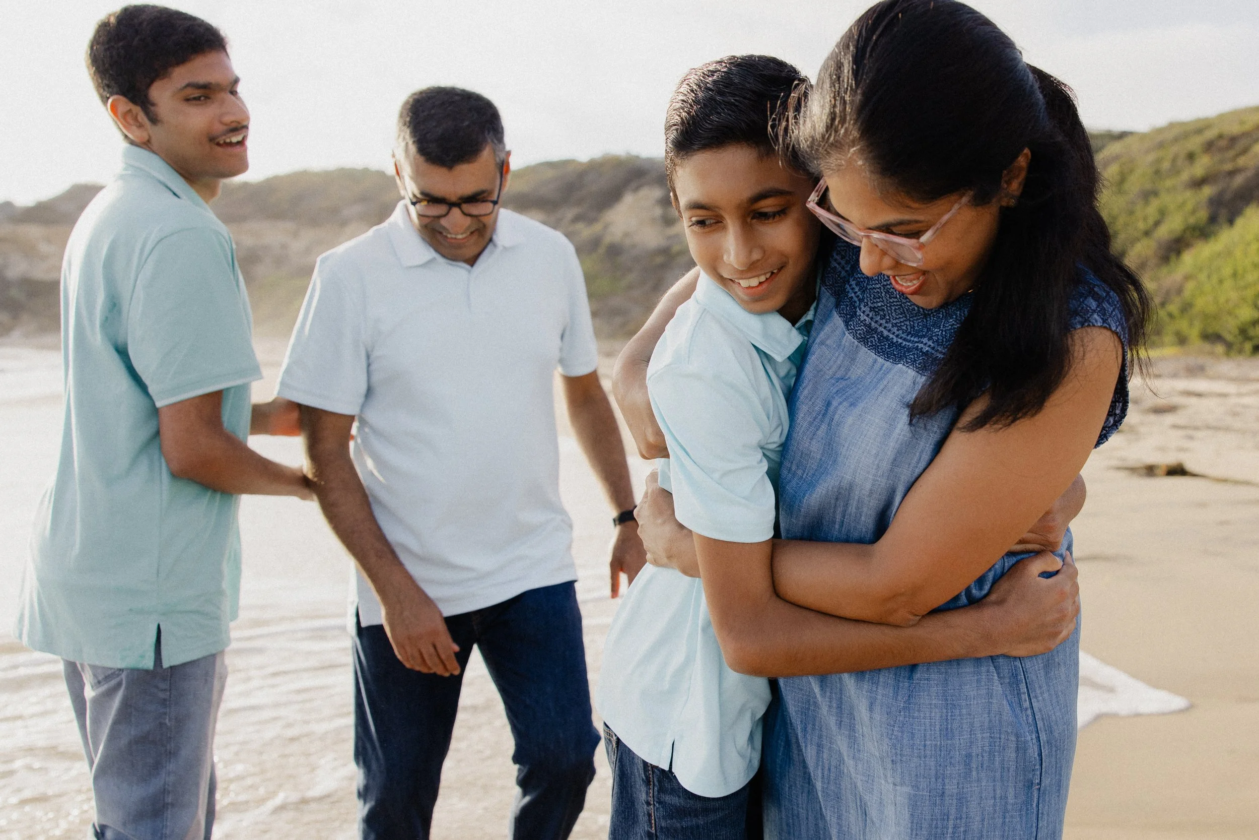 A mother and father hugging their two teenage sons on the beach at Crystal Cove State Park during a relaxed family portrait session.