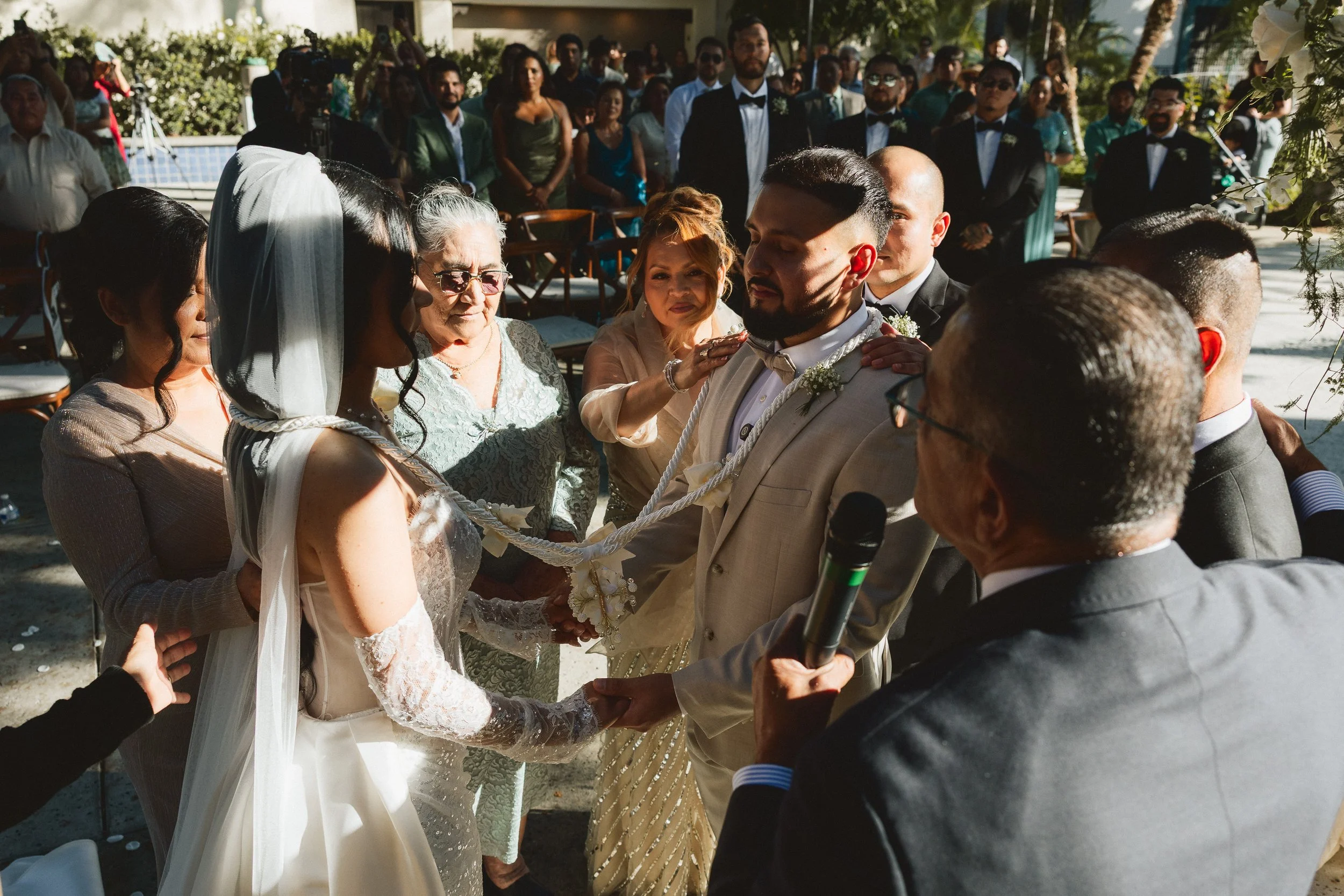 Family members placing lasso around bride and groom during Catholic-inspired ceremony at Los Angeles River Center and Gardens.