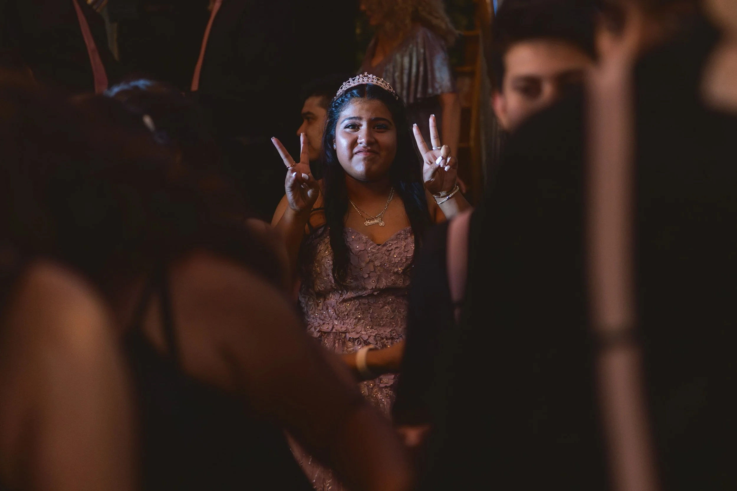 A candid moment of a Quinceañera wearing a tiara making peace signs on the dance floor.