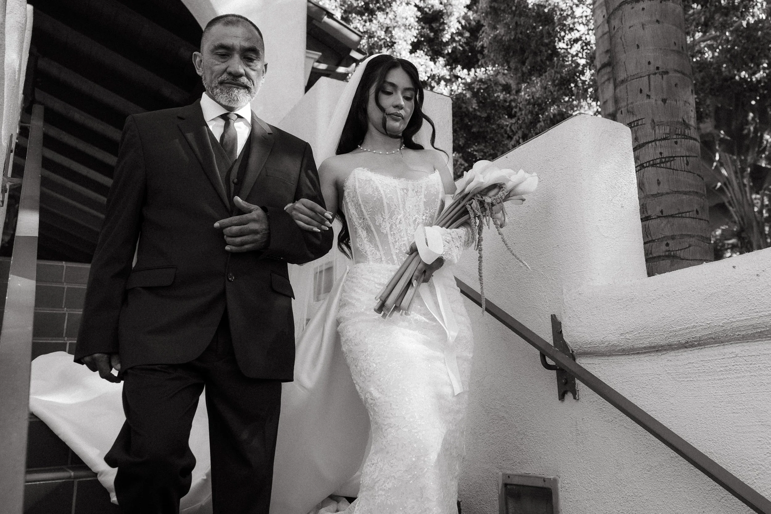 Bride walking arm in arm with her father holding calla lily bouquet