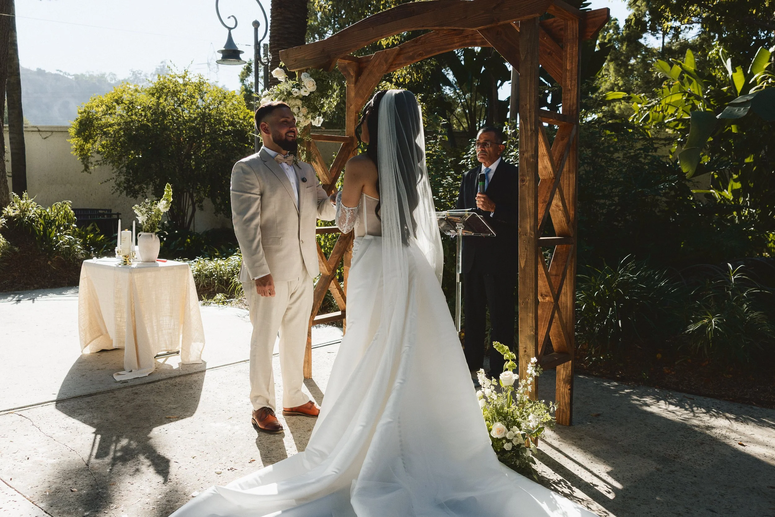 Bride and groom exchanging vows under wooden arch at Los Angeles River Center and Gardens.