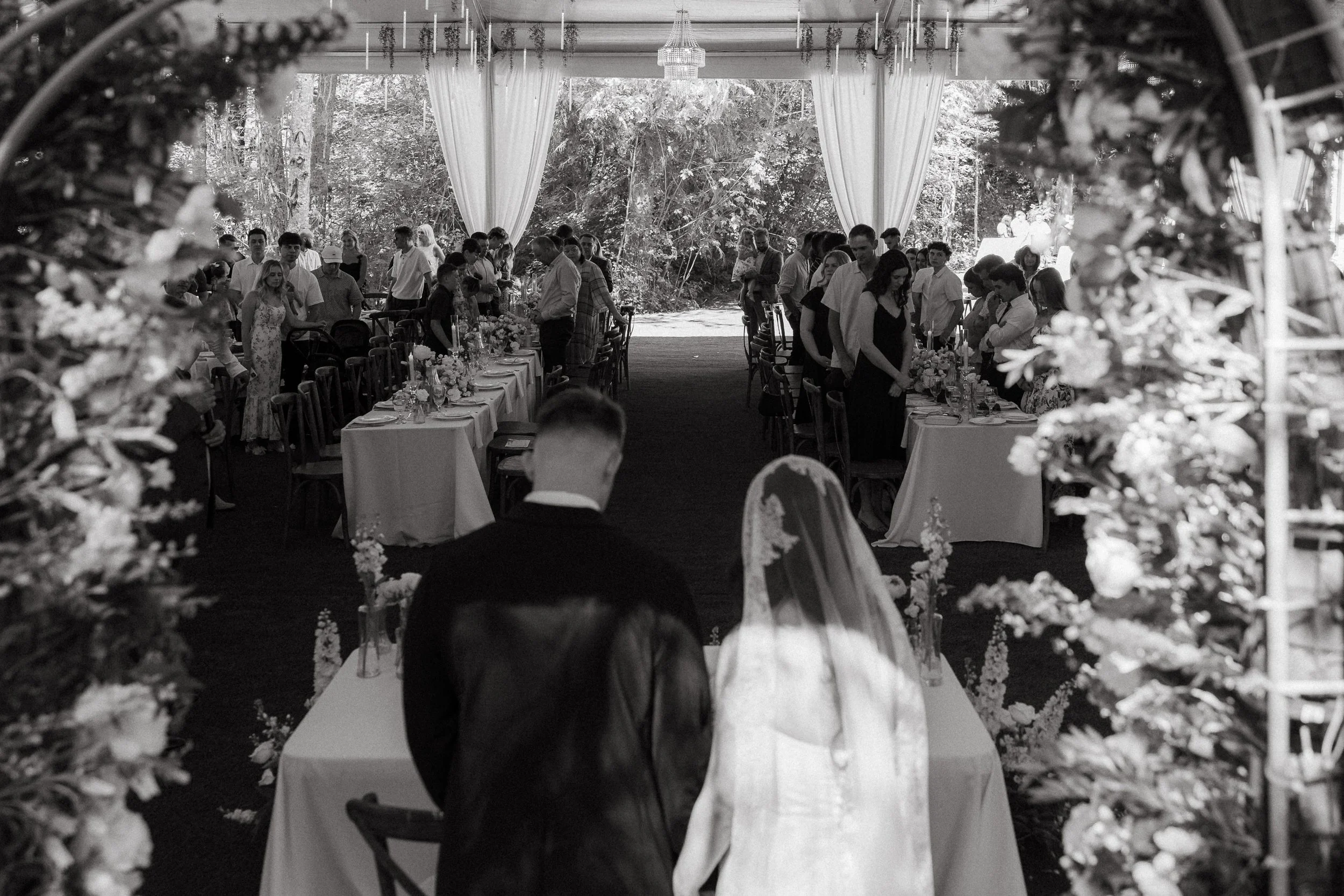 Bride and groom enter the floral-decorated tent reception from the back