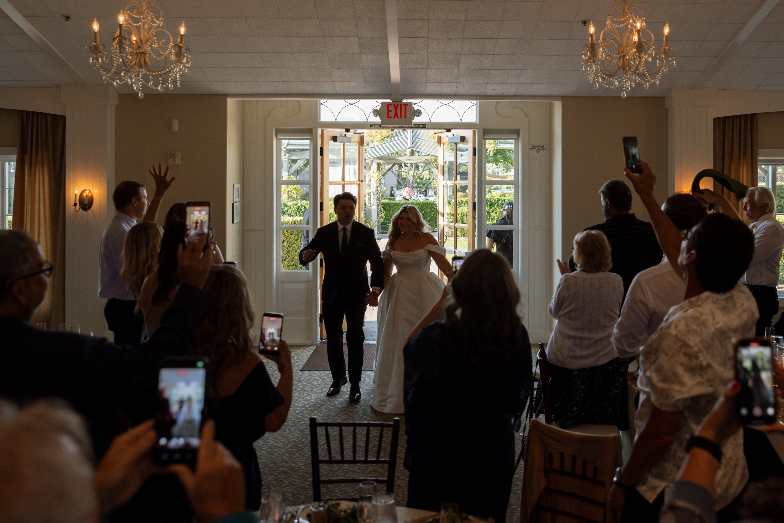 Bride and groom enter their reception to cheering guests through open doors