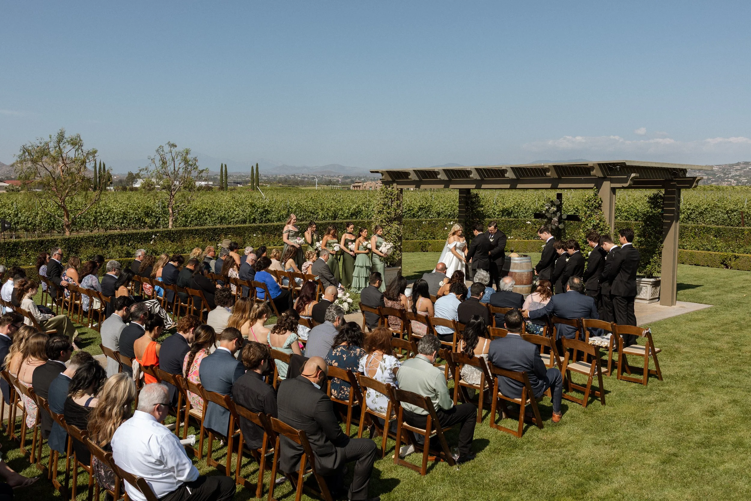 Wide view of the vineyard ceremony with guests seated and mountains beyond