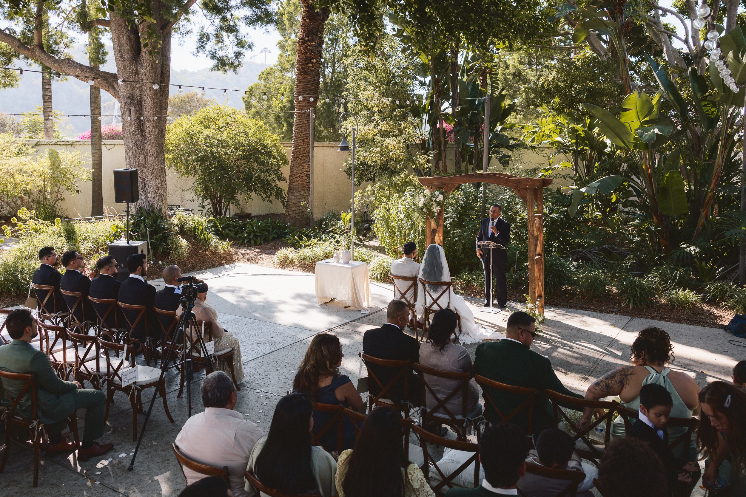 Wedding officiant speaking under wooden arch during ceremony at Los Angeles River Center and Gardens.