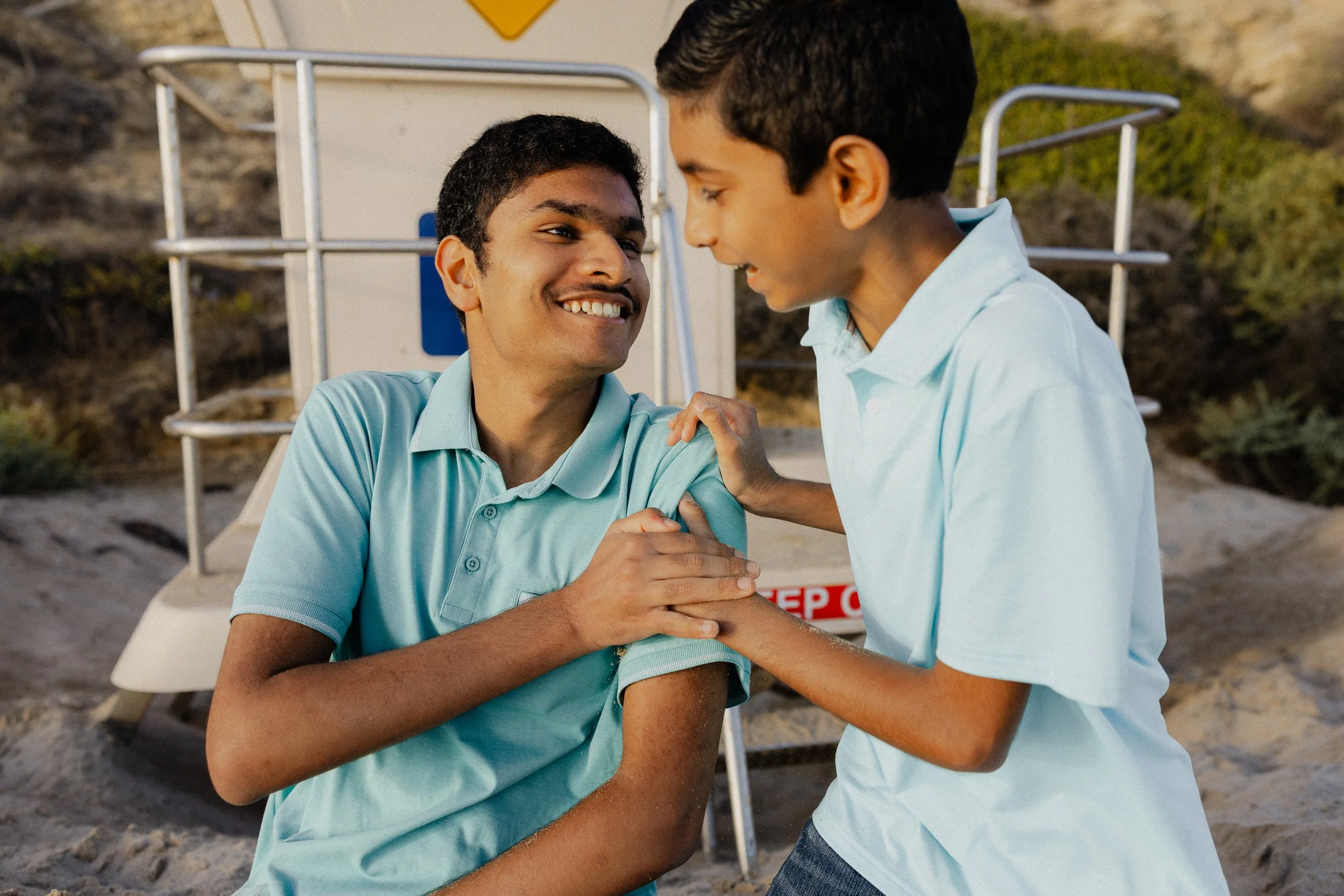 Candid moment of two brothers laughing and playing together near a lifeguard tower at Crystal Cove.