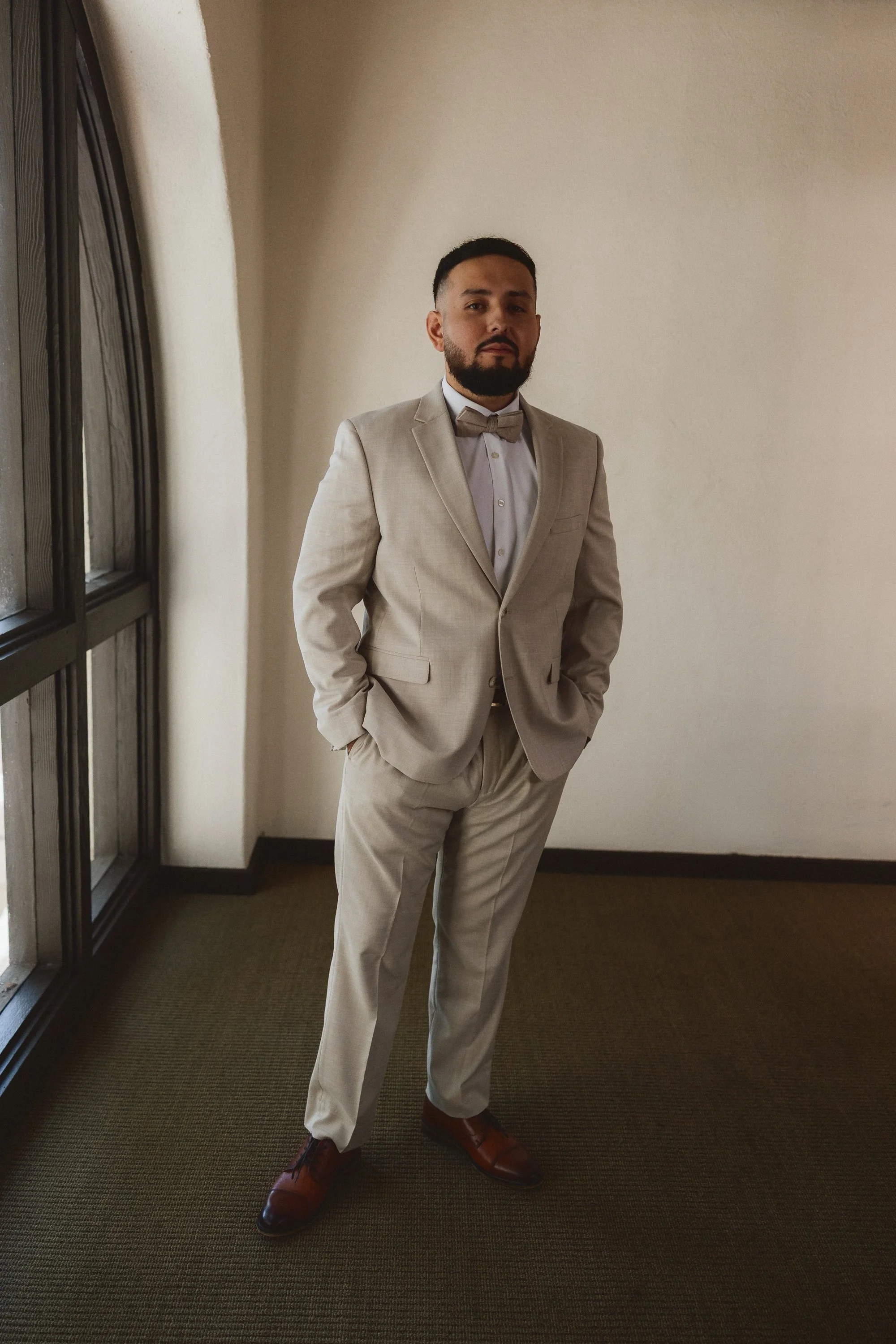 Groom in light suit standing by arched window at Los Angeles River Center