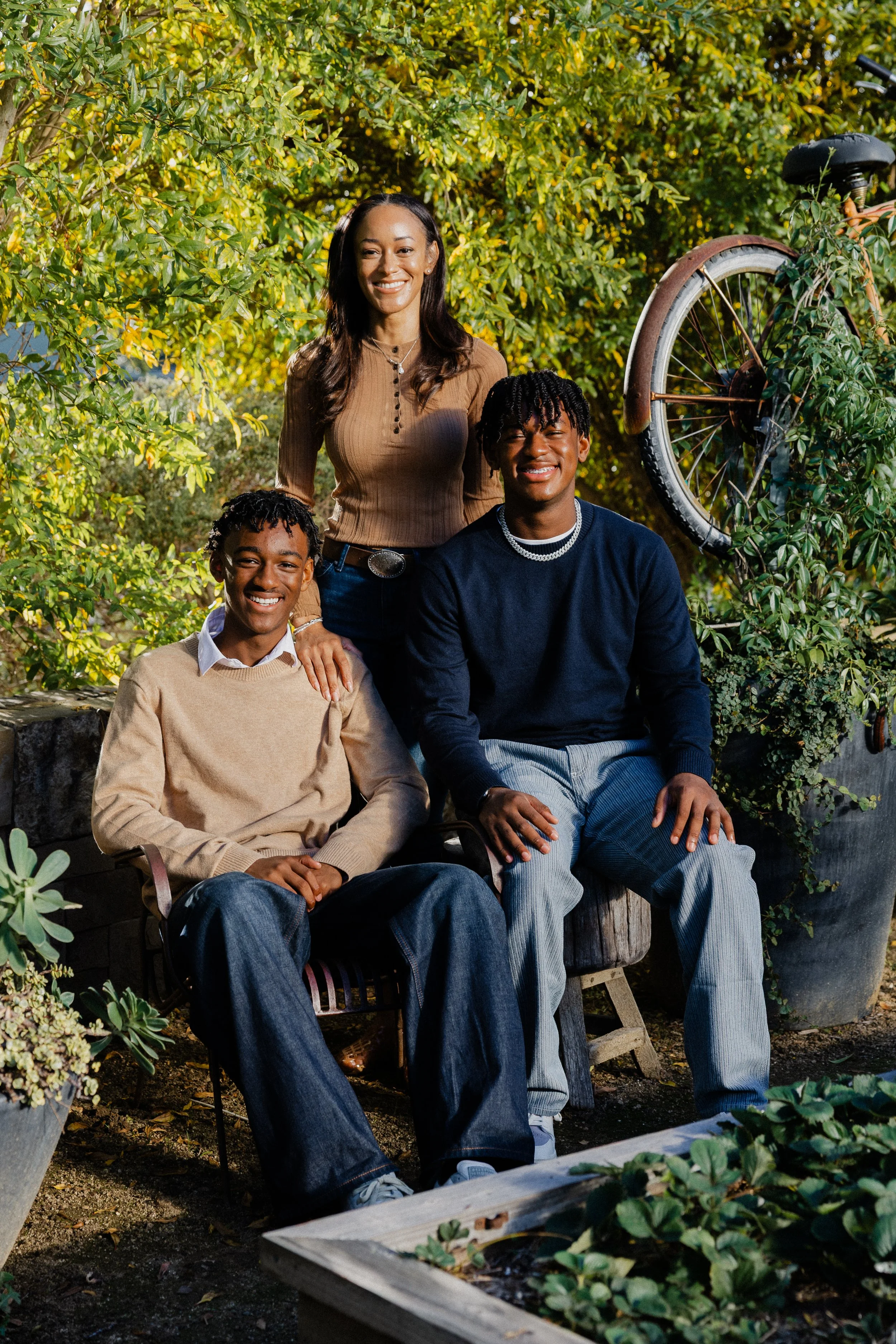 A holiday family portrait of Ashley standing behind her two sons seated on a rustic garden bench at Pavilion Park.