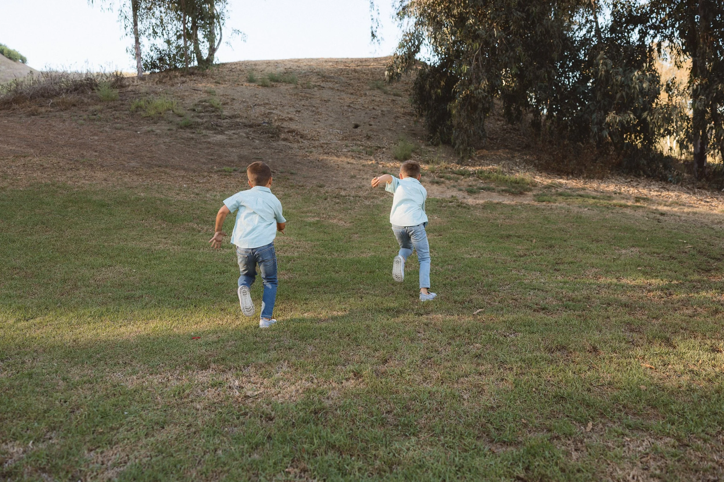 Two boys in jeans running up a big hill in Laguna Niguel.