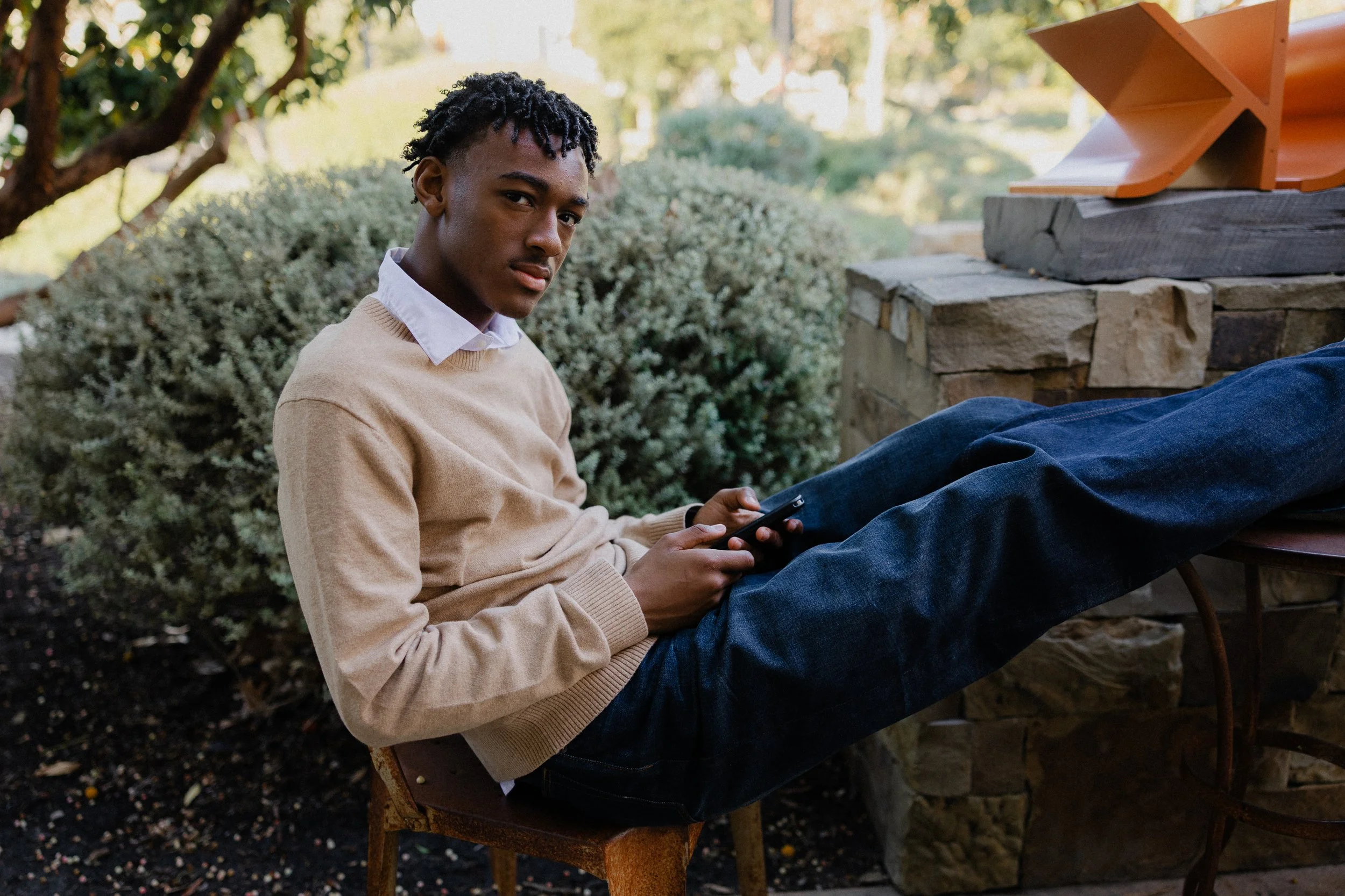 Teenage boy in a beige sweater sitting relaxed with his legs propped up on a stone wall at Pavilion Park.