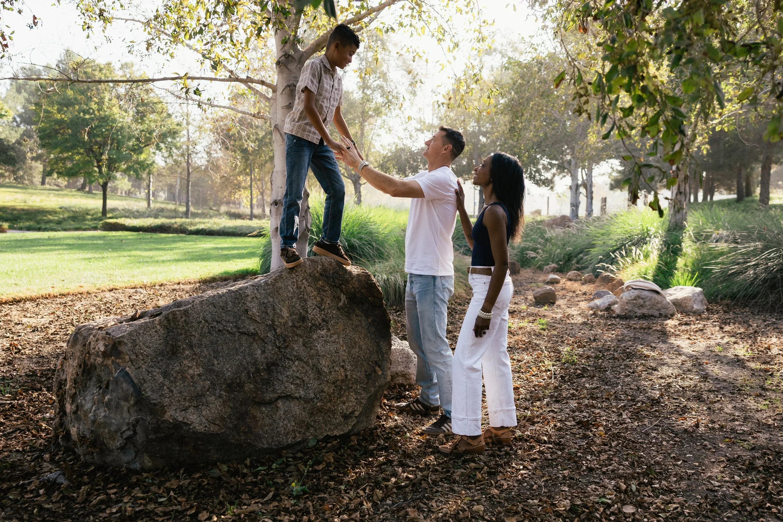 A family of four standing on large boulders under trees during a sunny afternoon session at Jeffrey Open Space Trail in Irvine.