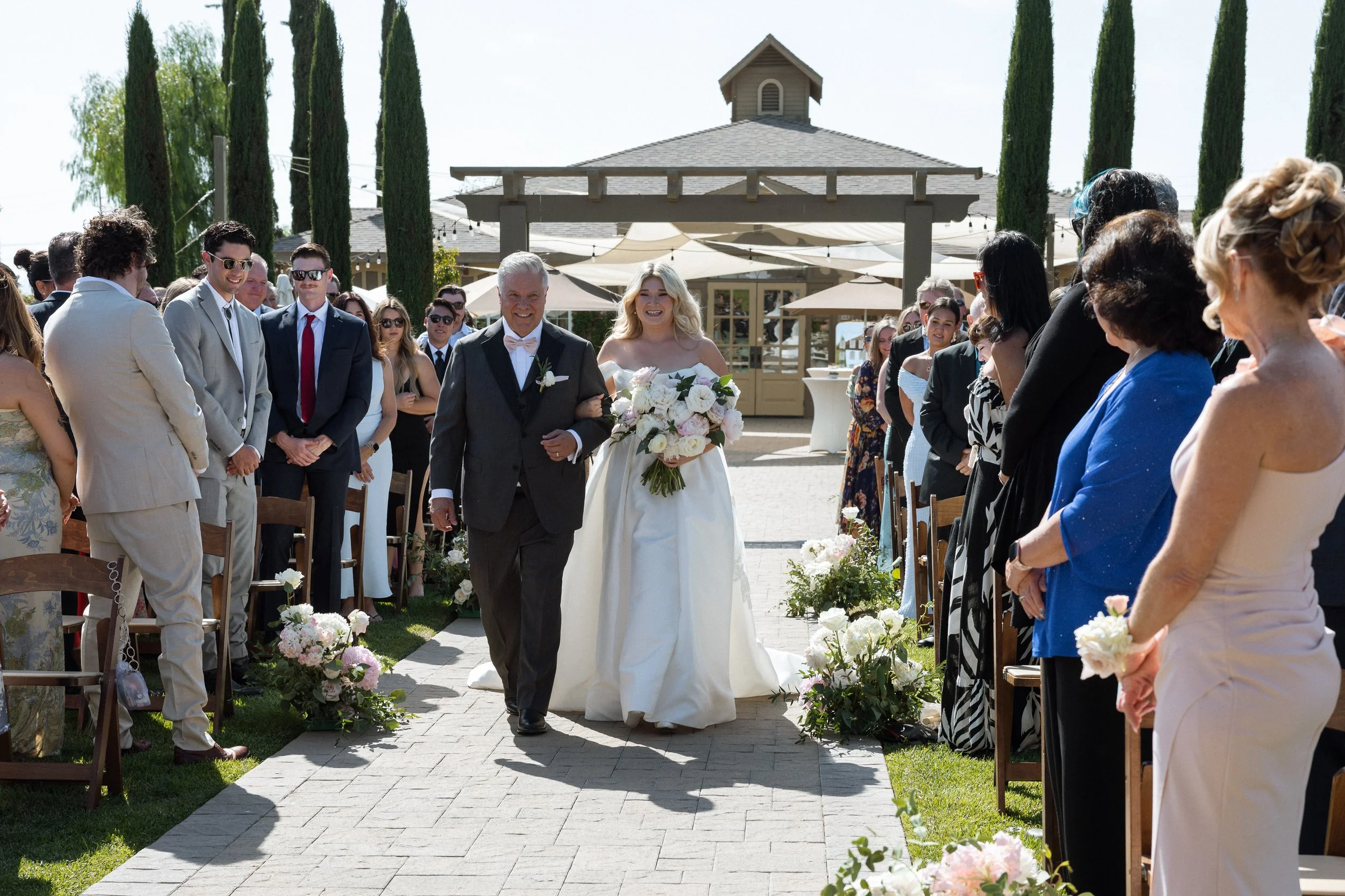 Bride walks down the aisle on her father's arm as guests stand and watch