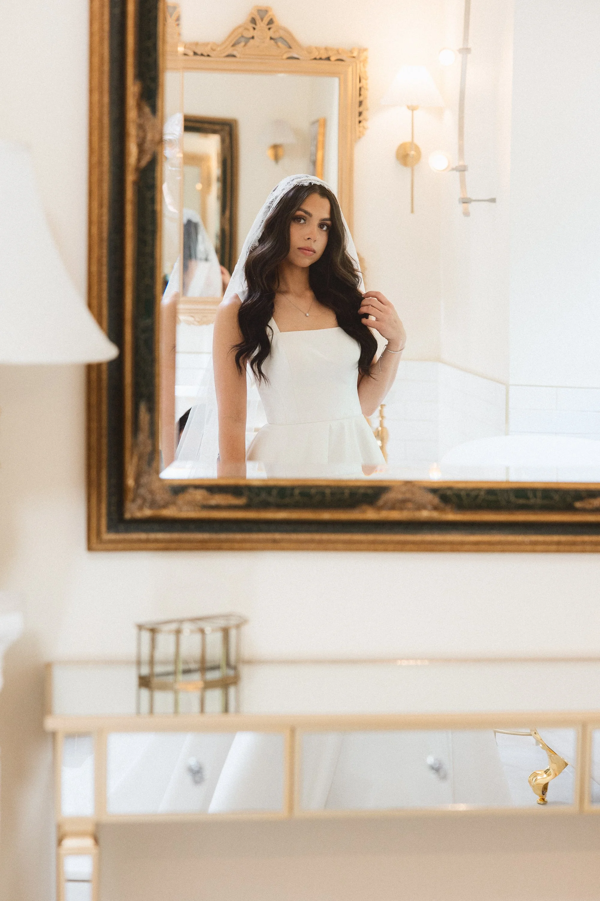 Bride looking at her reflection in a gold-framed mirror while getting ready for the wedding.