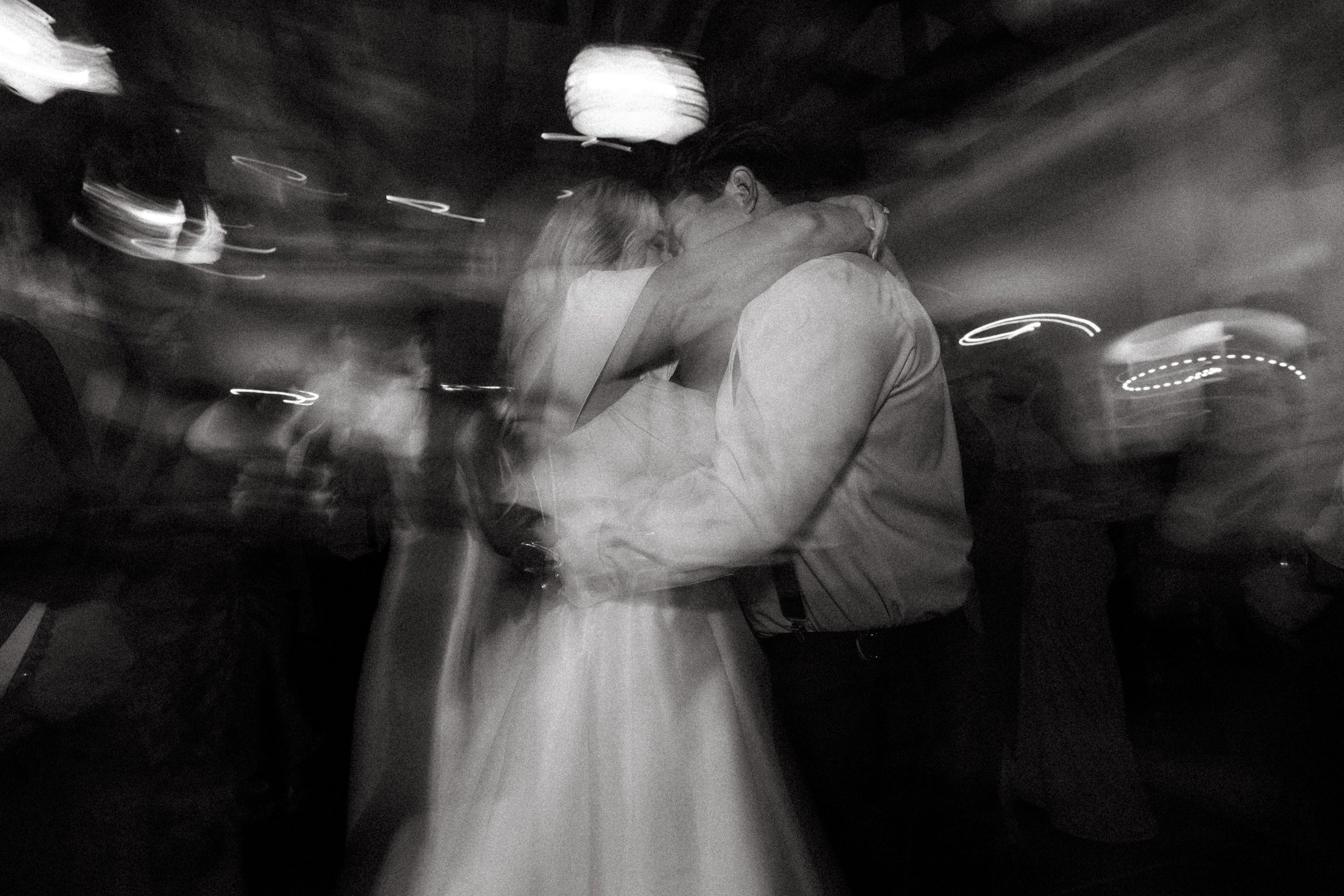 Bride and groom kiss on the dance floor amid swirling motion-blur light trails