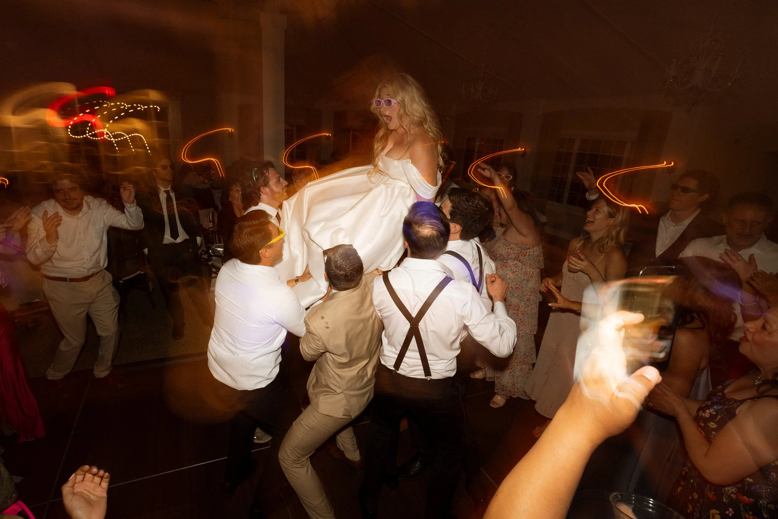 Bride is lifted up on a chair by cheering guests during the reception