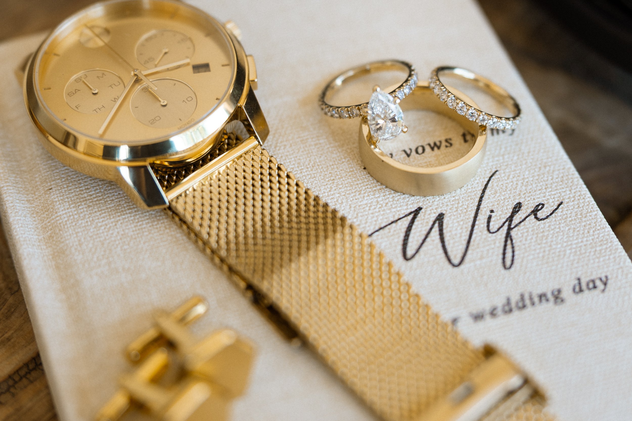 Gold watch, cufflinks, and wedding rings resting on a vow book