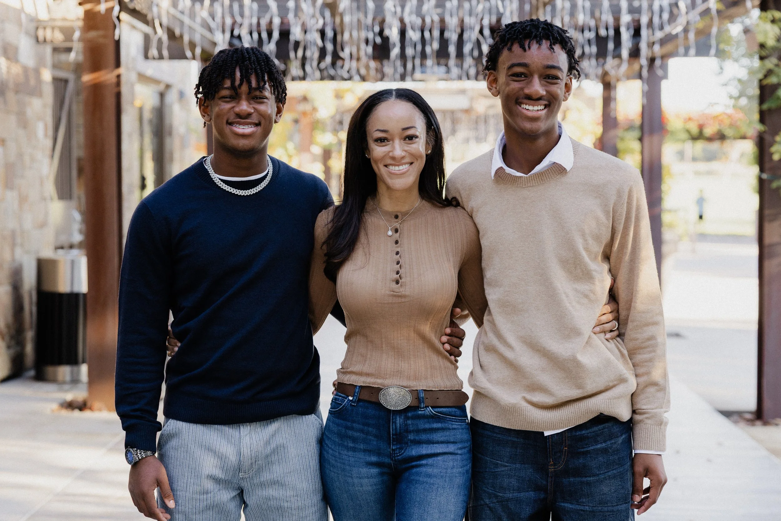 Ashley standing arm-in-arm with her two teenage sons, Blaze and Blake, under string lights during a holiday session in Irvine.