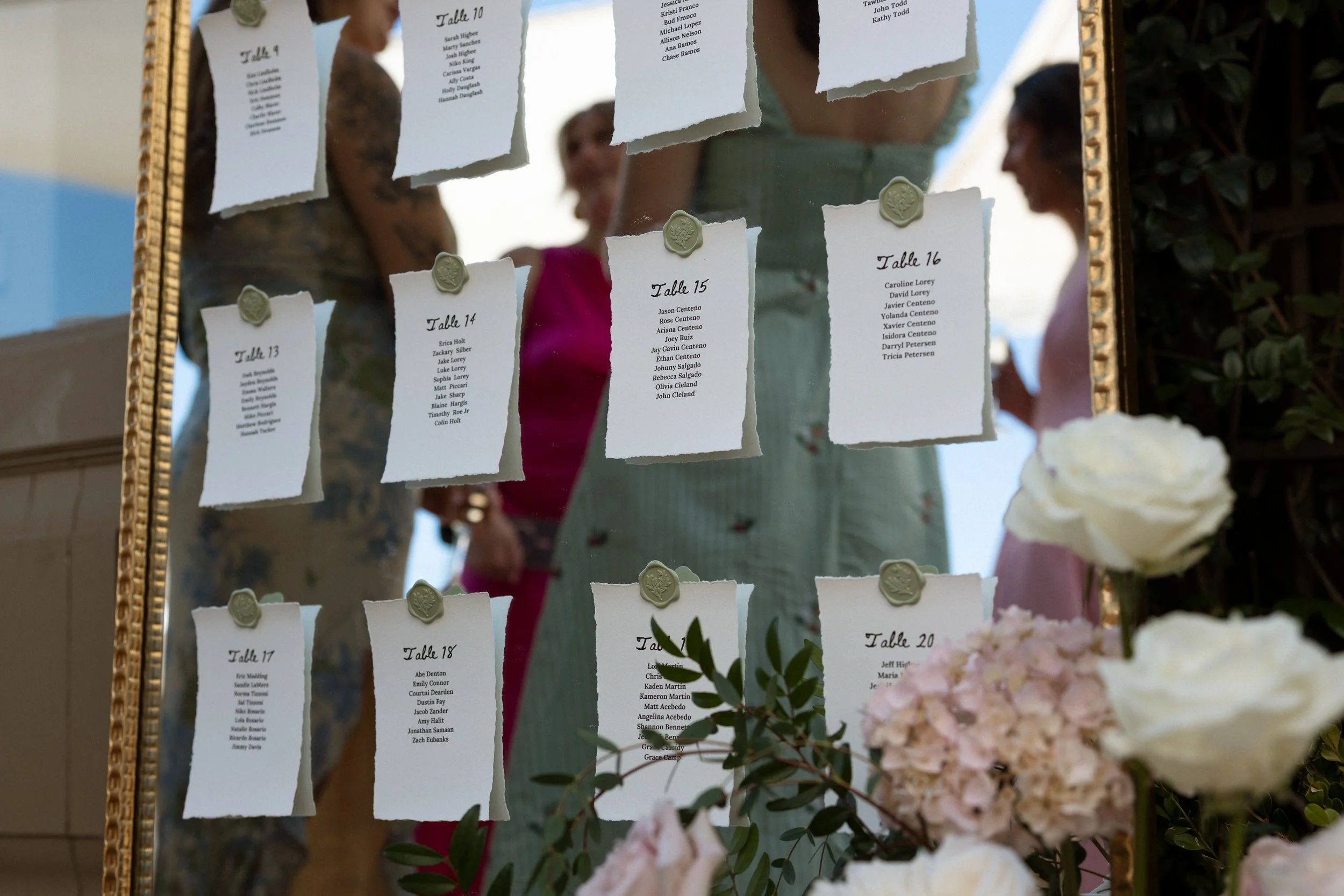 Guests reflected in a gold mirror displaying handwritten table seating cards