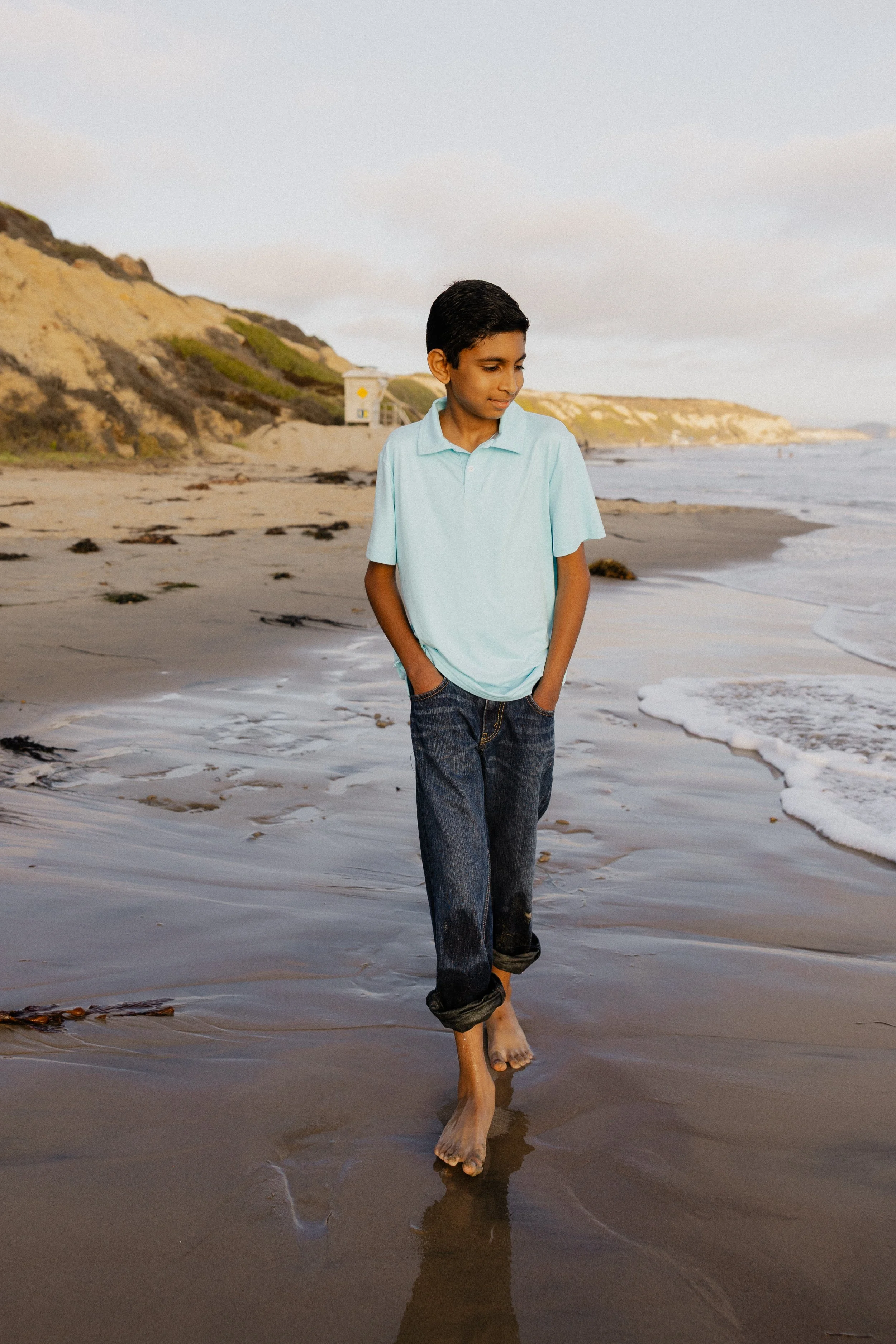 Black and white portrait of a young boy walking barefoot along Crystal Cove beach shoreline.