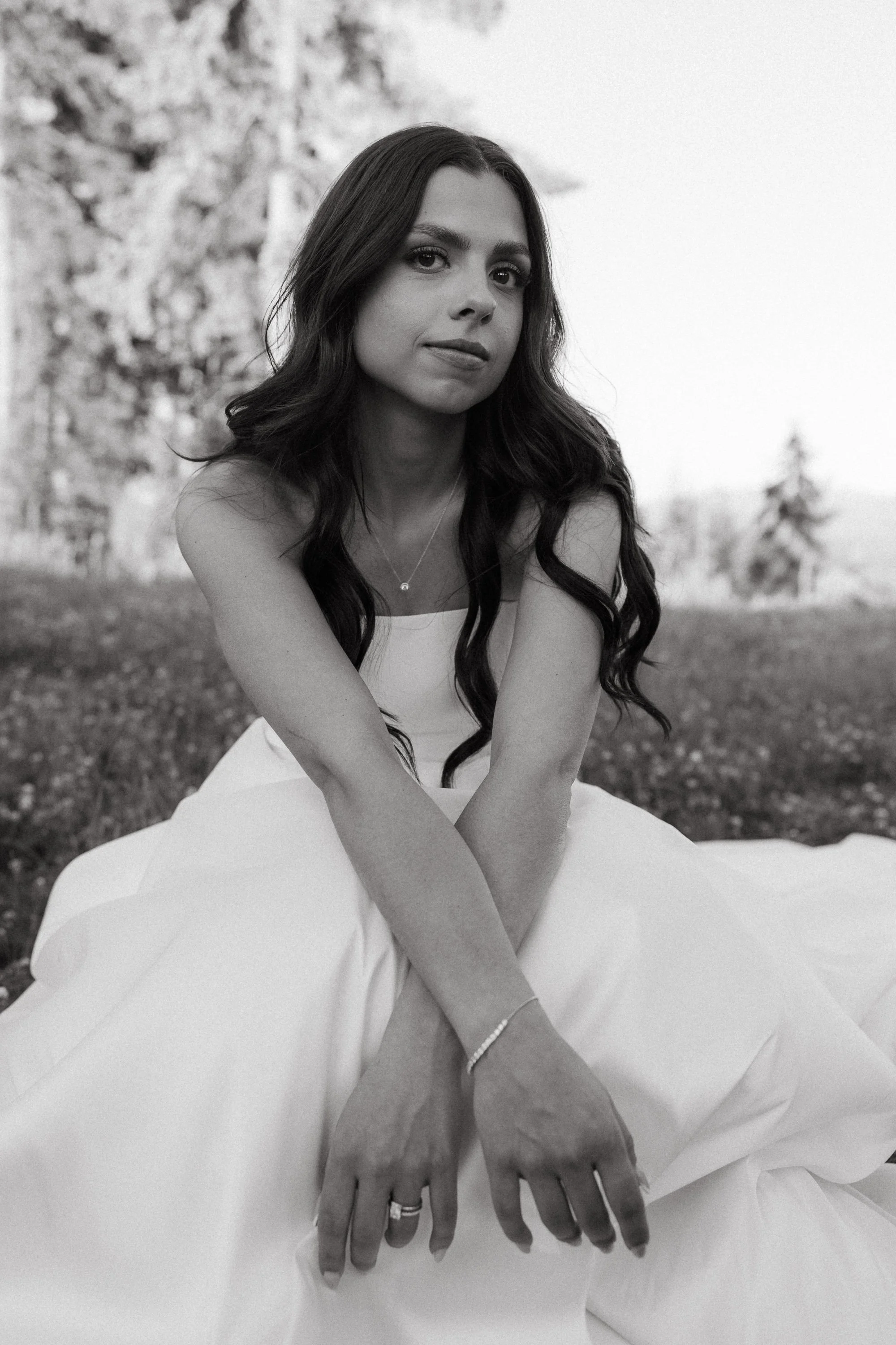 Black and white portrait of the bride sitting in a field, looking into the camera with a calm expression.