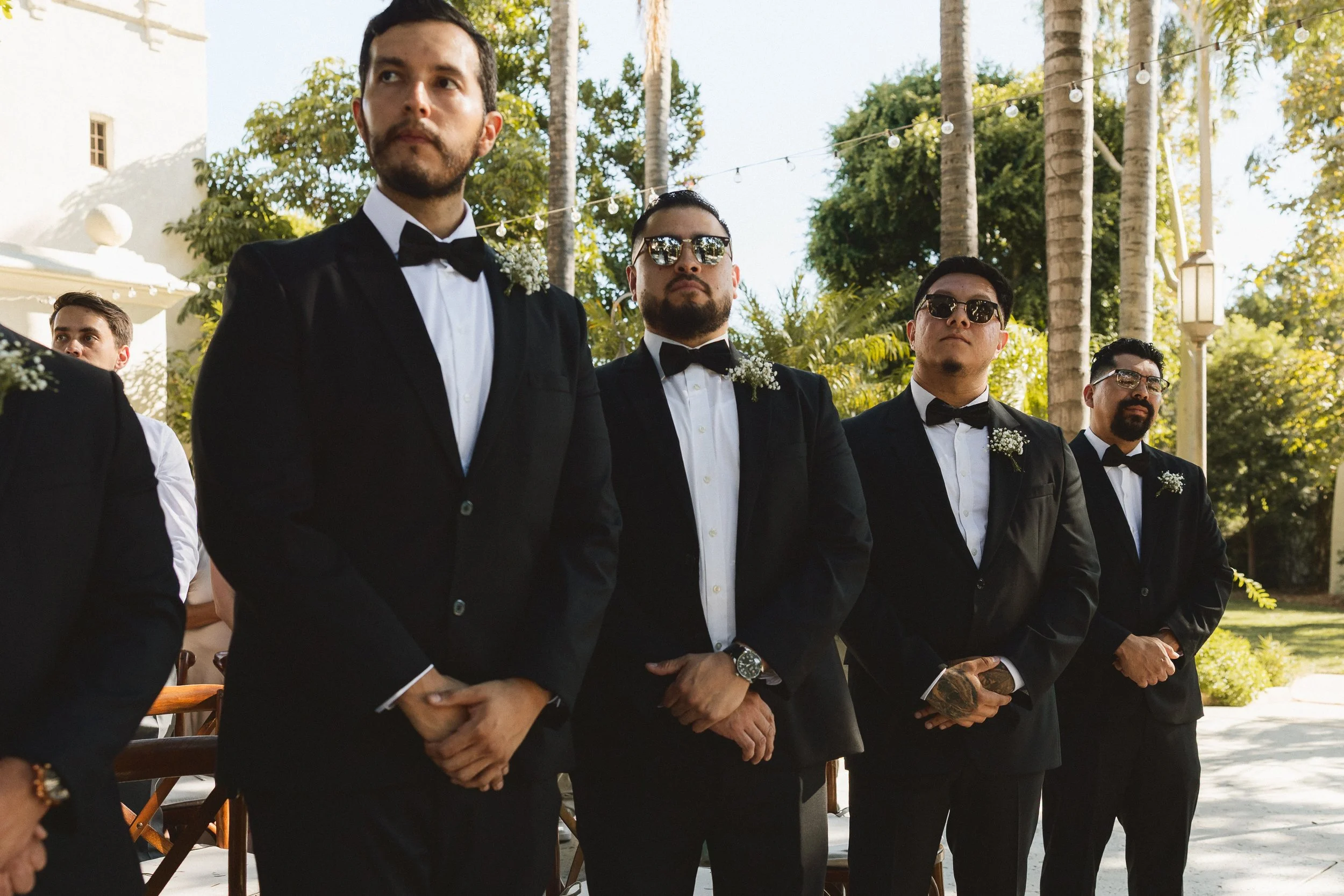 Groomsmen in black tuxedos standing together during ceremony at Los Angeles River Center and Gardens.