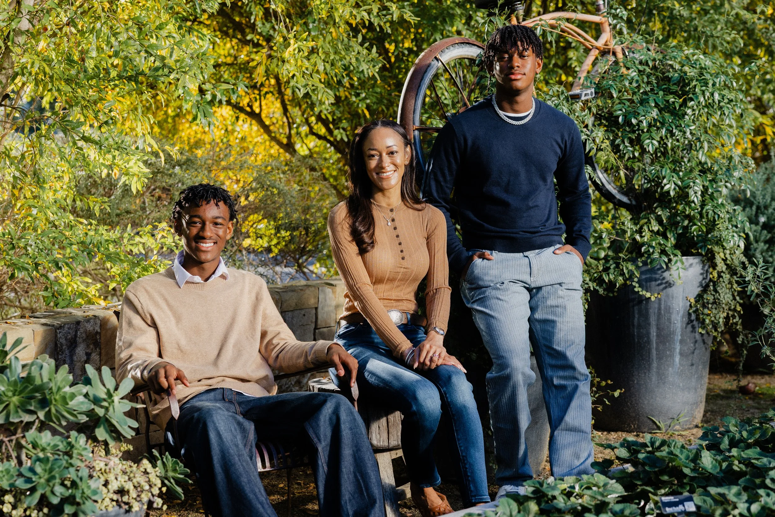 A holiday family portrait of Ashley standing behind her two sons seated on a rustic garden bench at Pavilion Park.