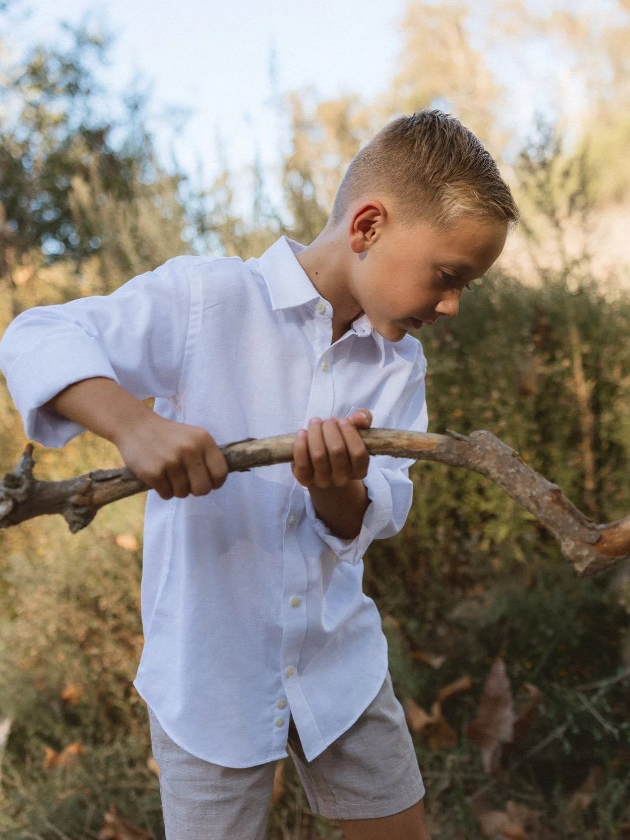 8 year old blond haired boy playing with a stick.