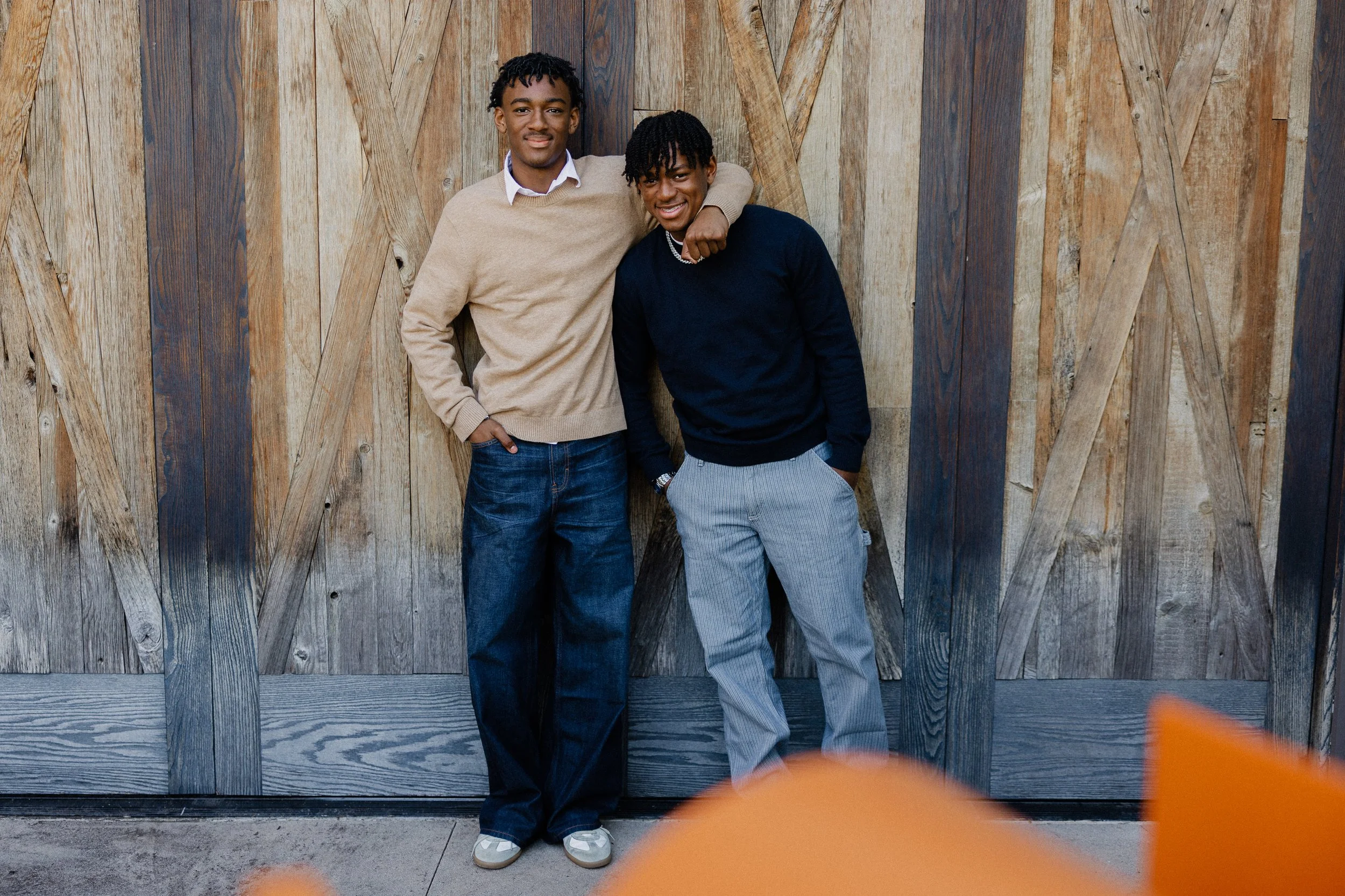 Two teenage brothers standing arm-in-arm against a large rustic wooden barn door at Pavilion Park in Irvine during a holiday session.