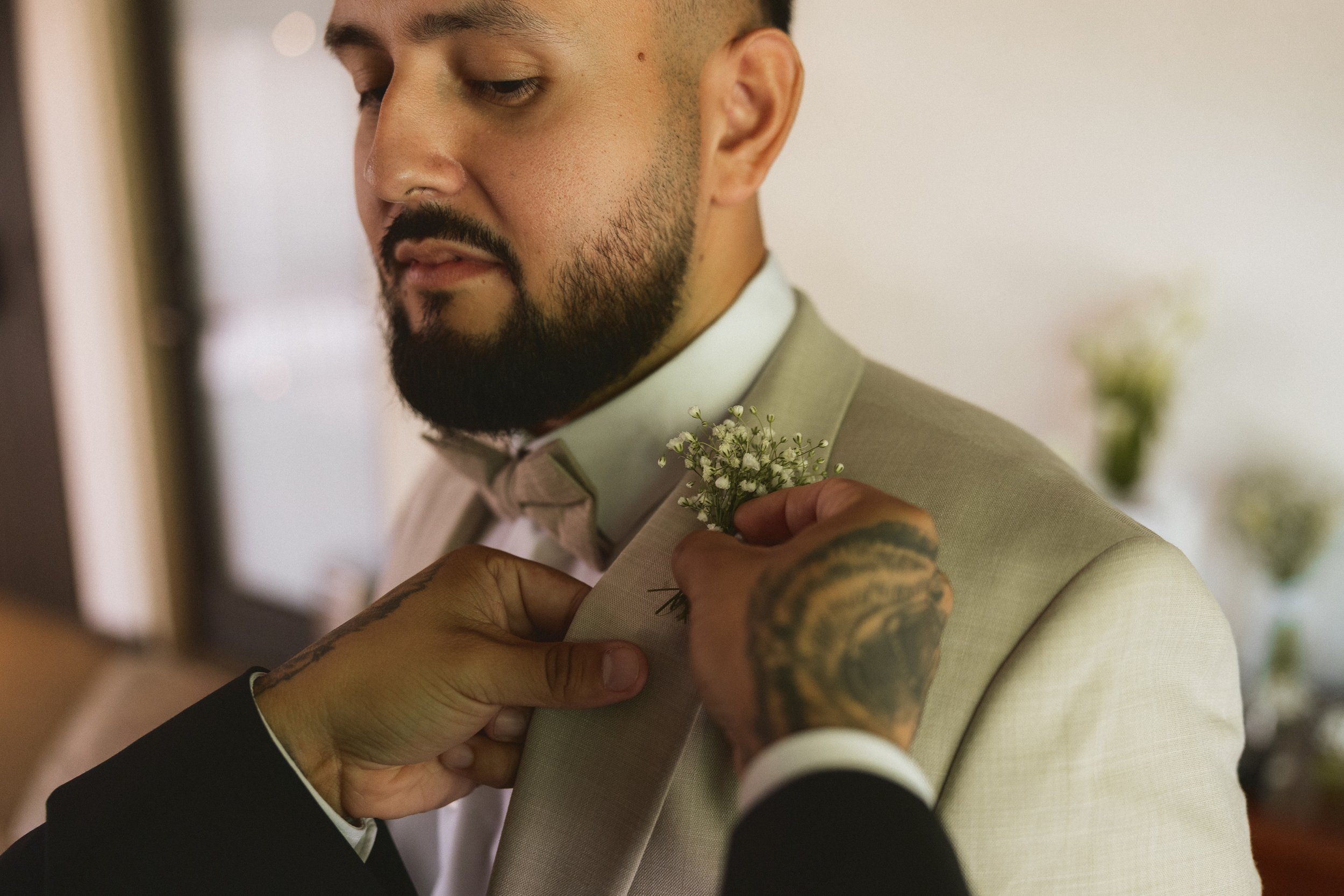 Close-up of groom having boutonniere pinned before ceremony