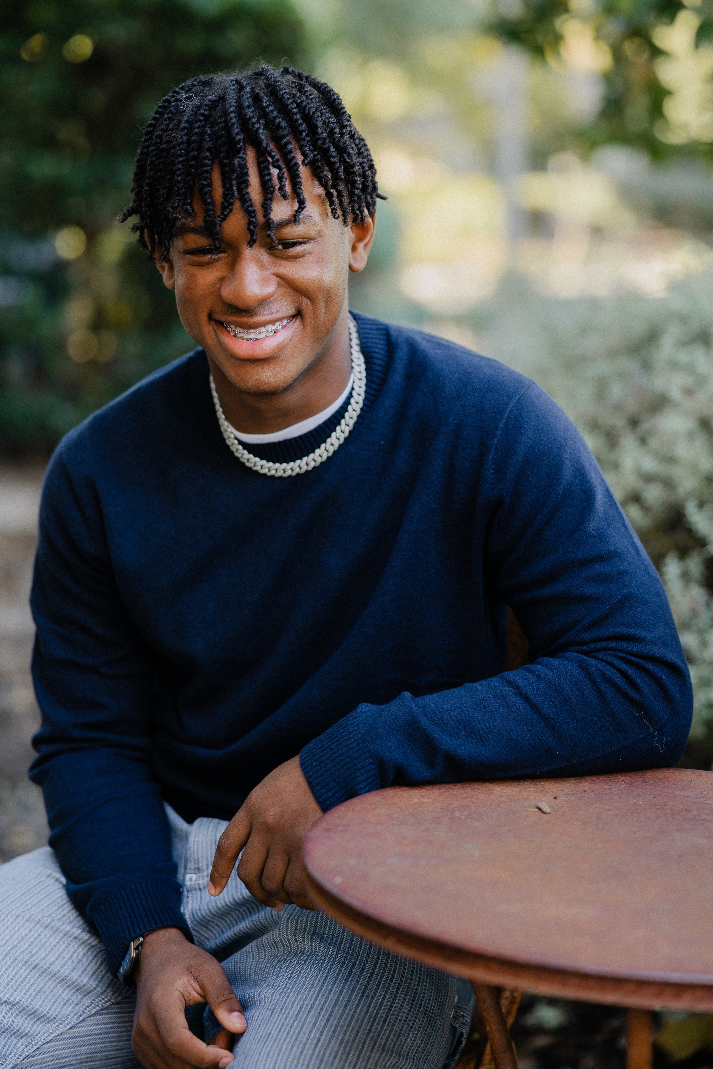 Candid portrait of a teenage boy laughing naturally while sitting at a rustic outdoor table.
