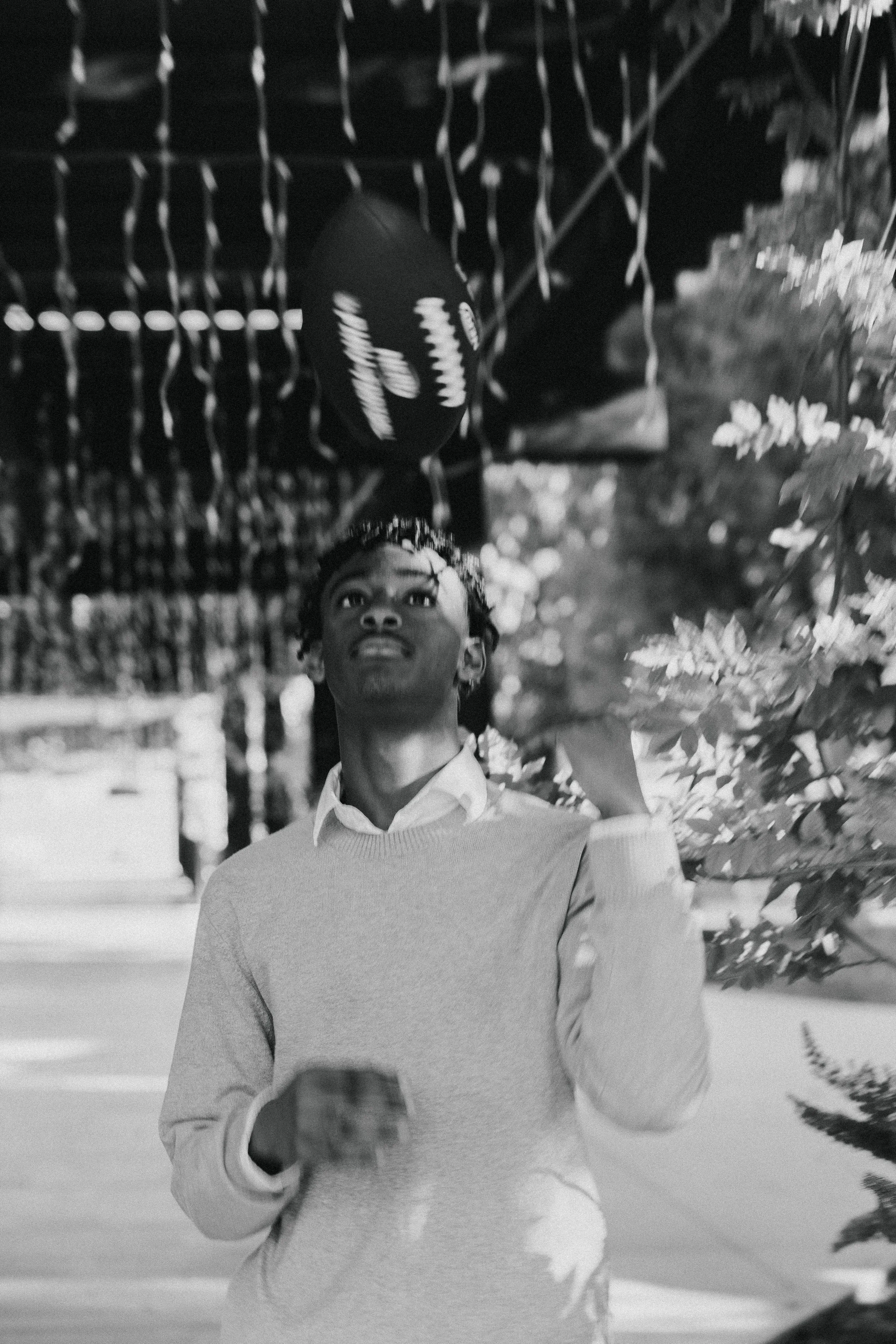 Artistic black and white photo of a teenage boy tossing a football in the air.
