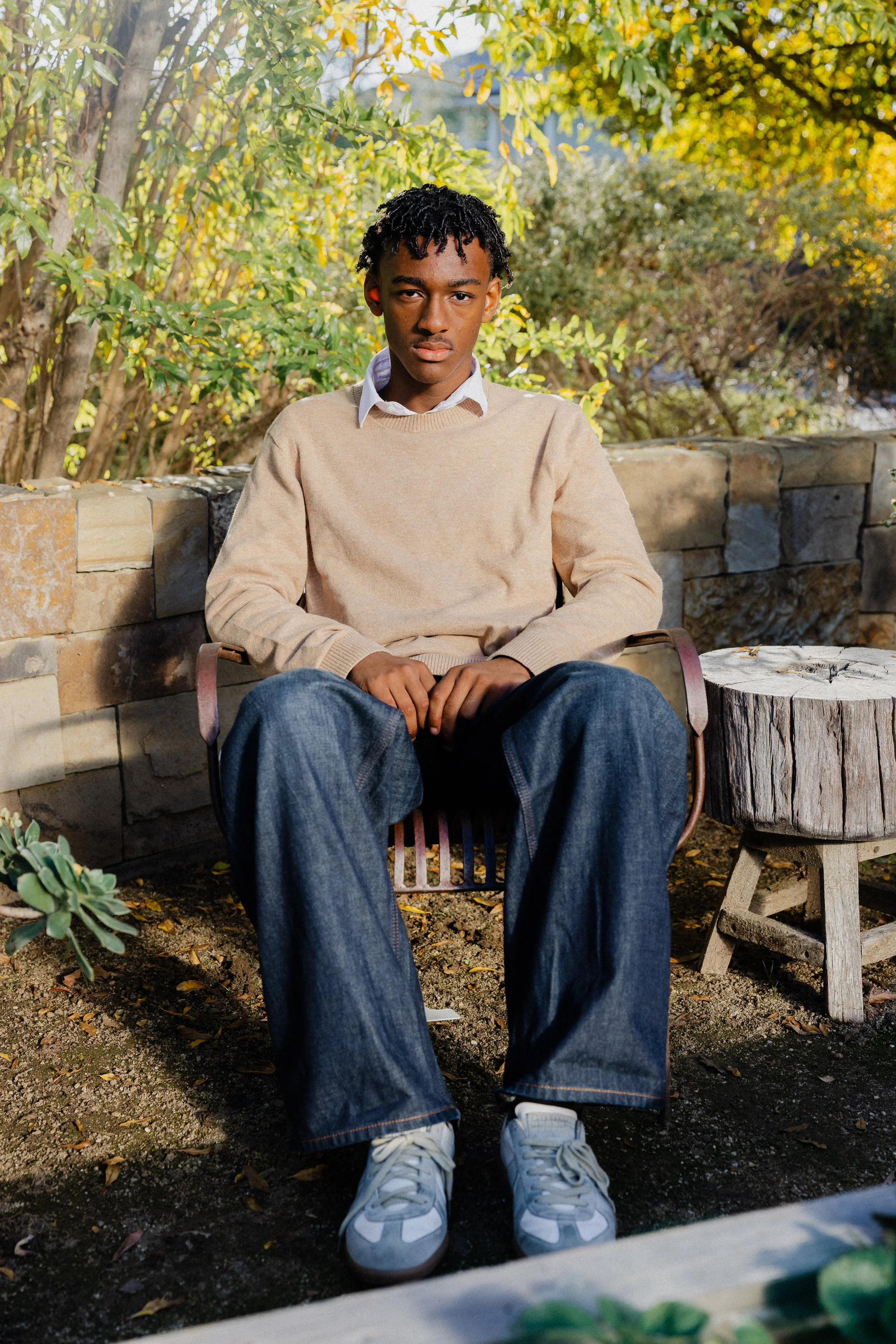 Serious portrait of a teenage boy sitting in a metal garden chair surrounded by fall greenery in Irvine.