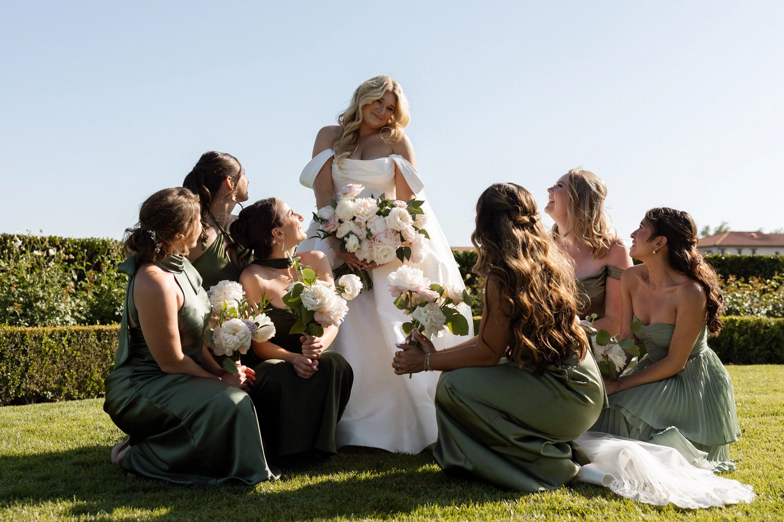 Bride laughing with bridesmaids gathered around her on the lawn