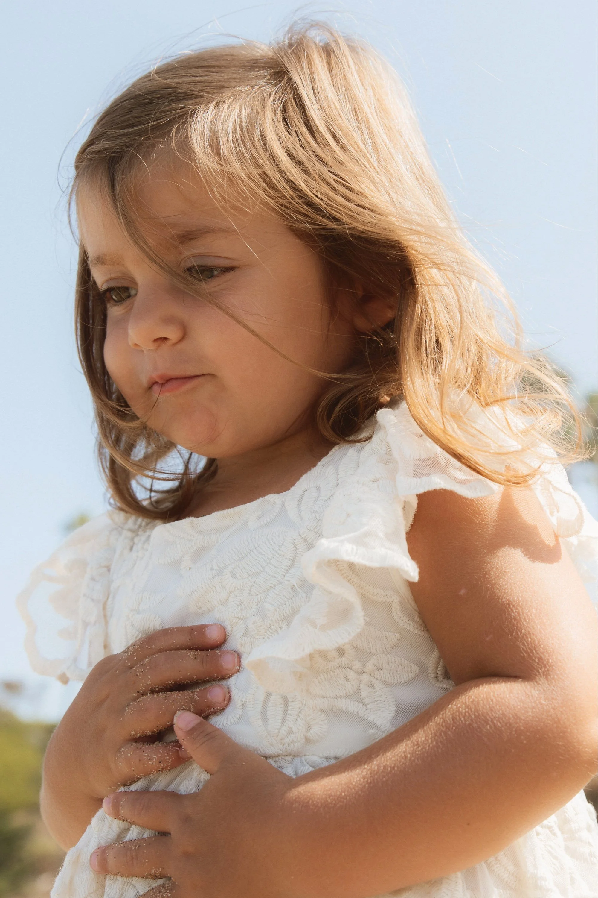 Playful young girl in a white dress holding sand on a sunny beach at Montage Resort & Spa.